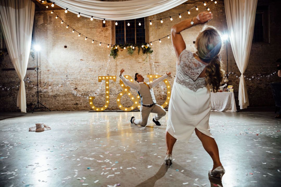 Wedding reception dance floor with string lights and white draping in an industrial venue.