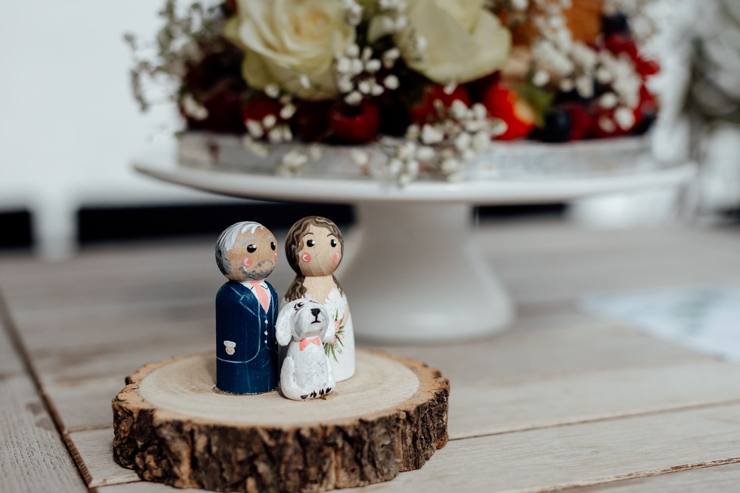 Cute bride and groom cake toppers displayed on rustic wood slice cake stands.