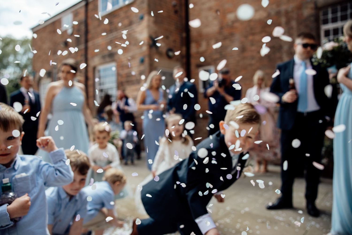 Wedding guests celebrate with confetti being thrown outside a brick building.