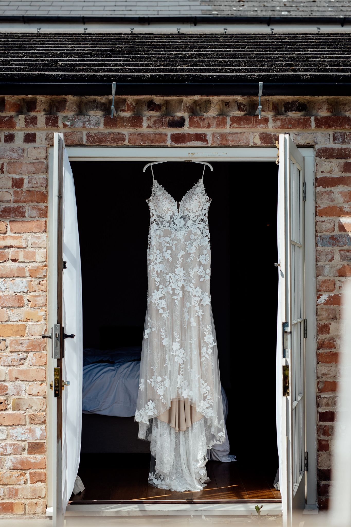 White lace wedding dresses hanging in windows against exposed brick wall.
