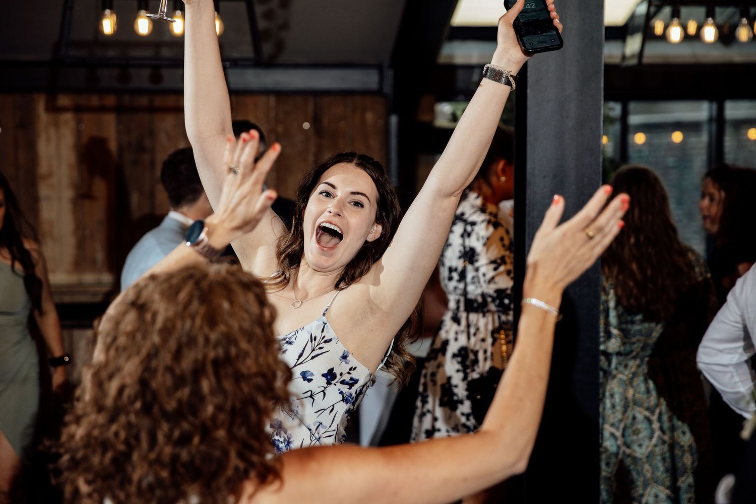 Wedding reception guests dancing and celebrating with raised arms.