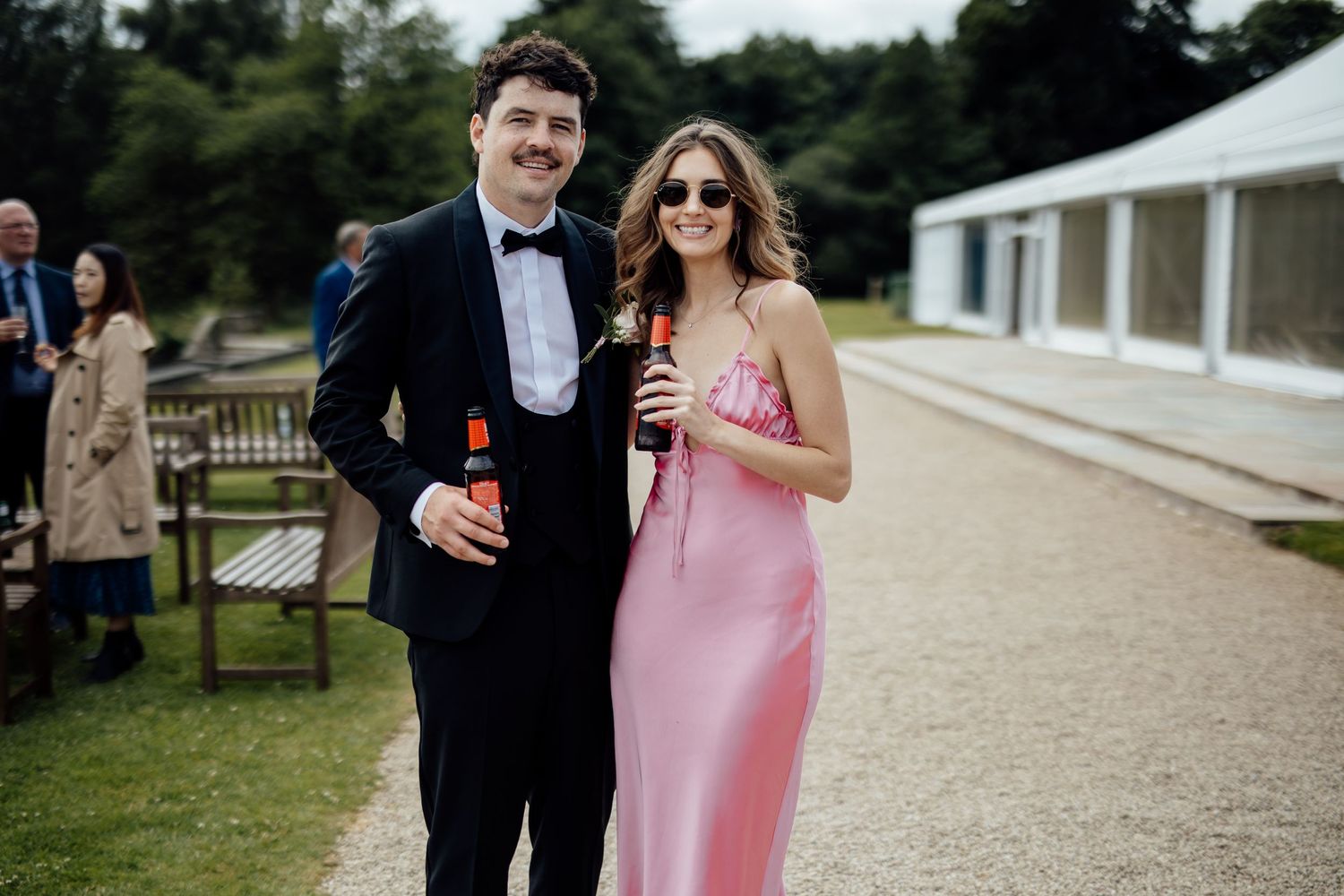 Wedding guests enjoying drinks at an outdoor reception with white tent in background.