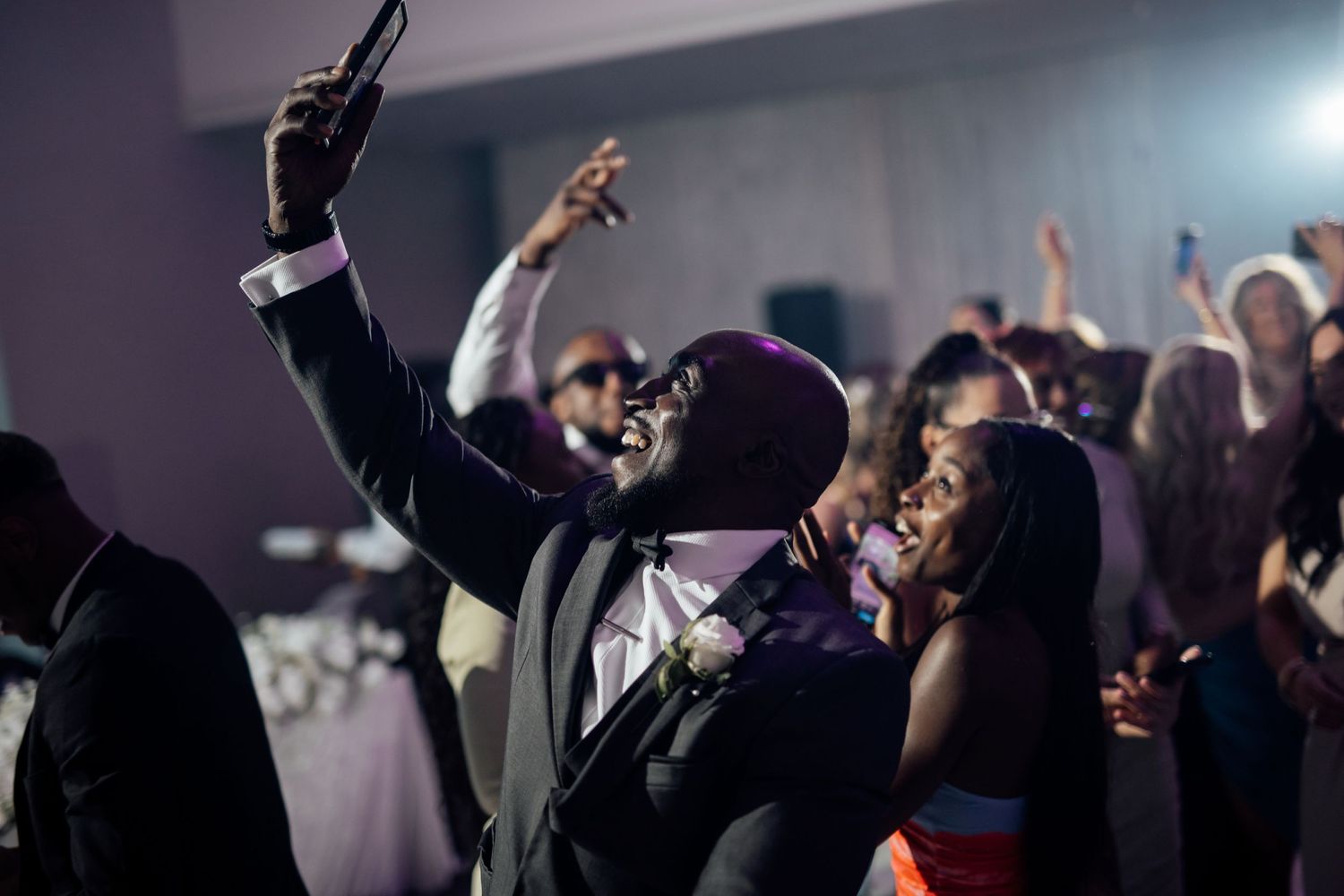 Energetic wedding reception dance party with guests on a dark dance floor with blue lighting.