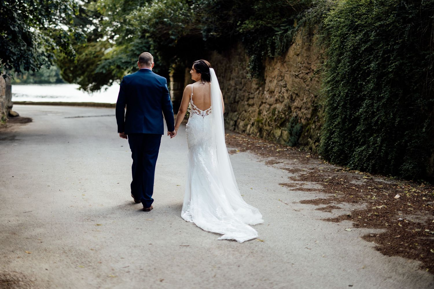 A wedding couple walking away down a scenic path with stone walls.