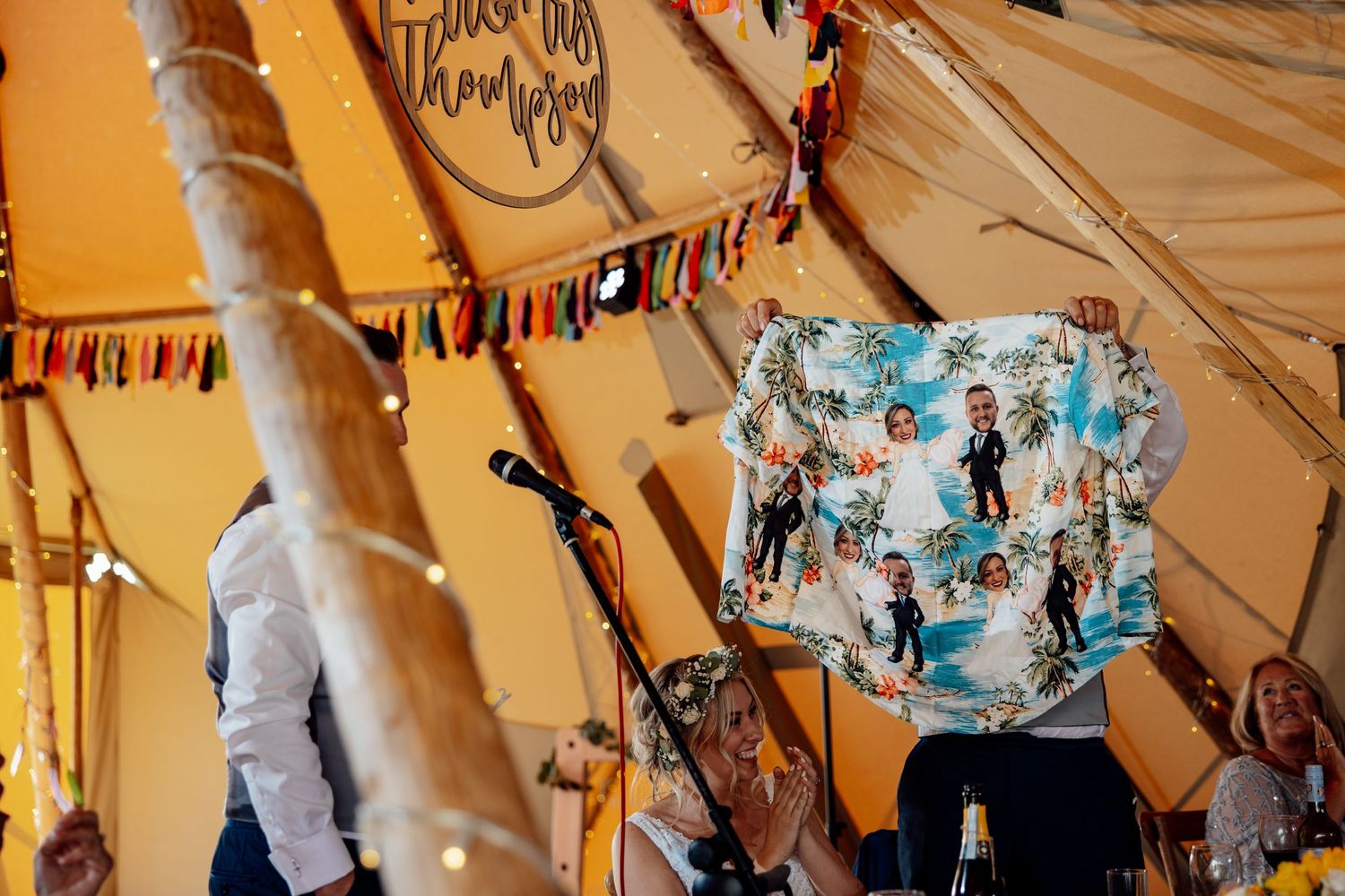 Hawaiian shirt being held up during celebration inside festive tipi tent.