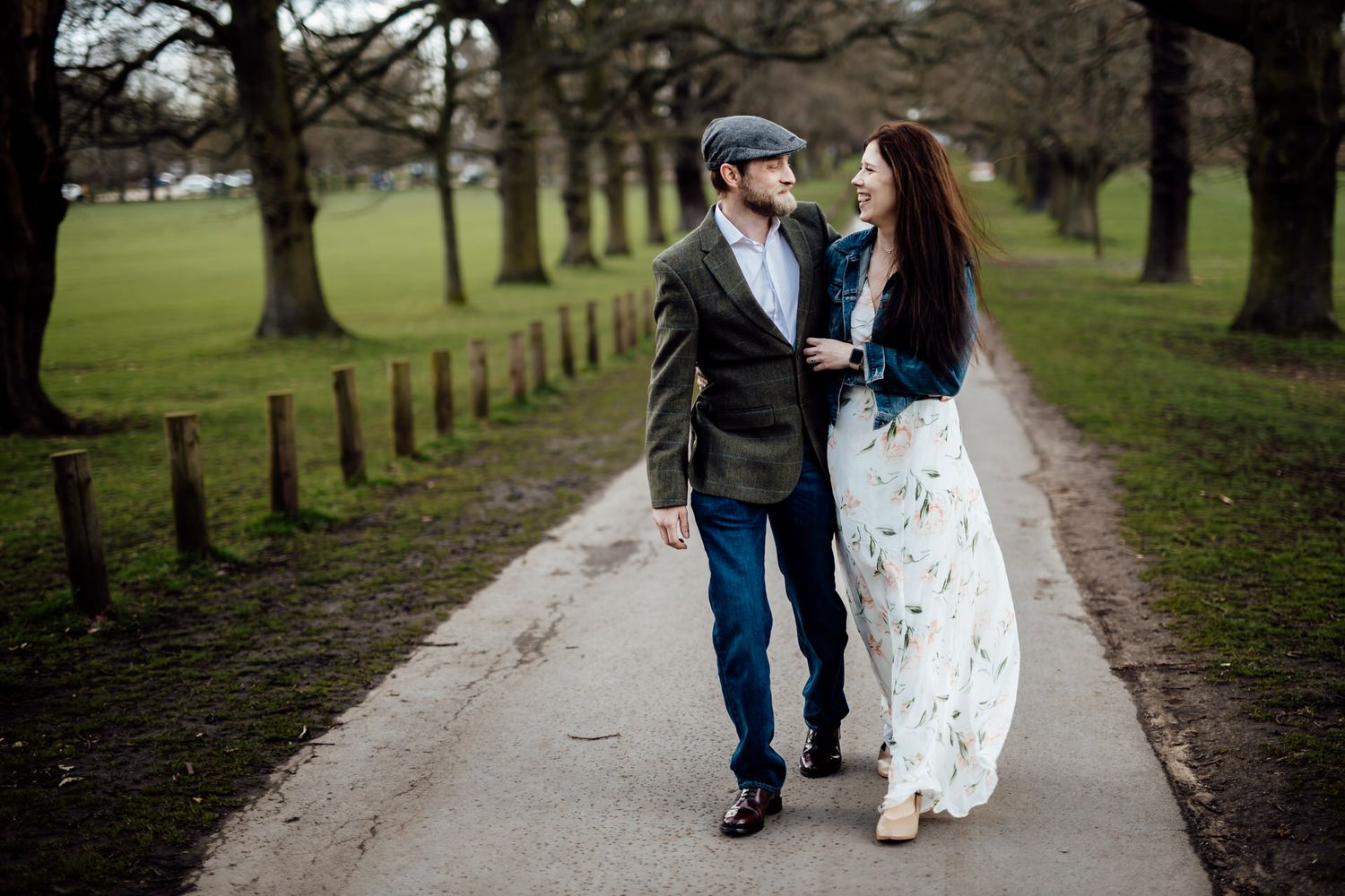 Couple strolling hand in hand along tree-lined path in park.