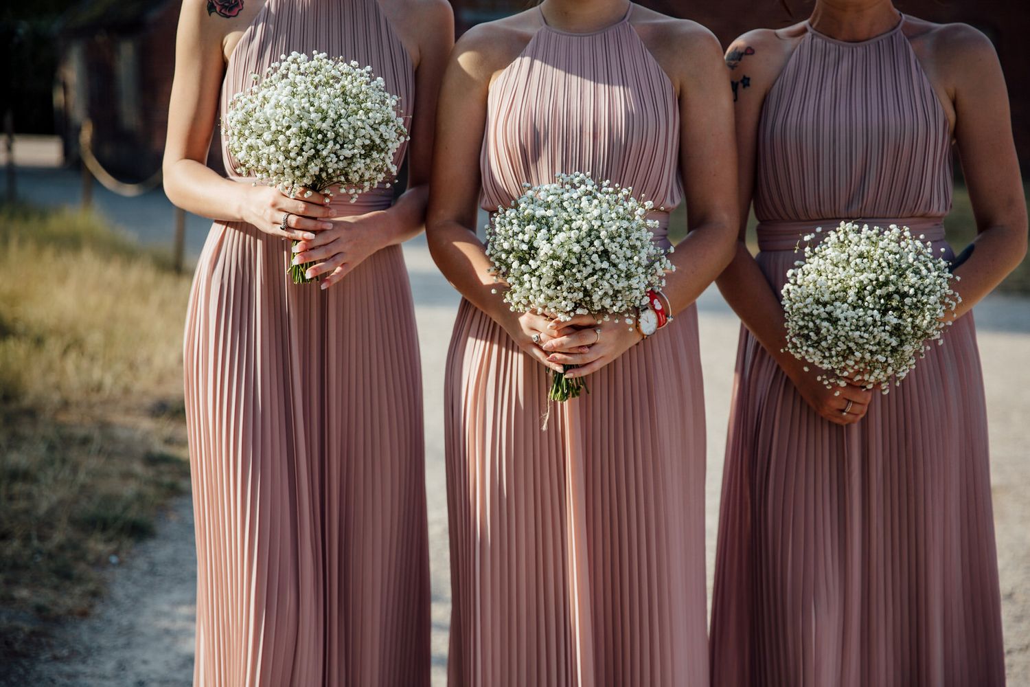 Bridesmaids in dusty rose pleated dresses holding baby's breath bouquets.