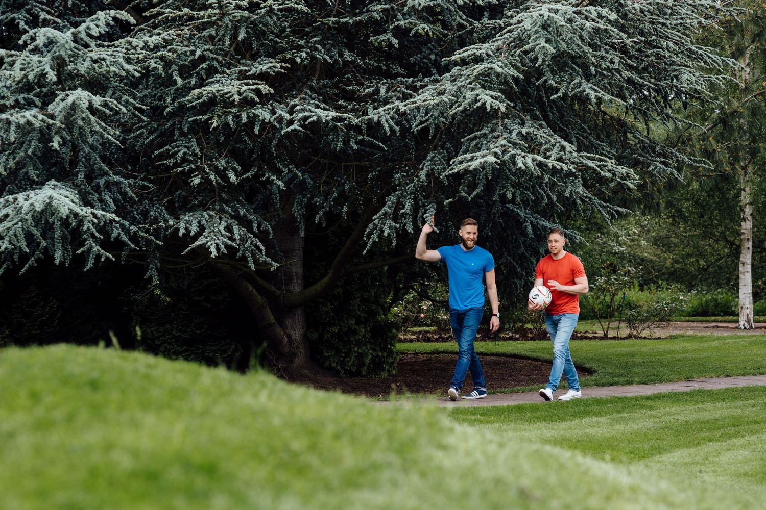 People walking through a garden path with evergreen trees in the background.