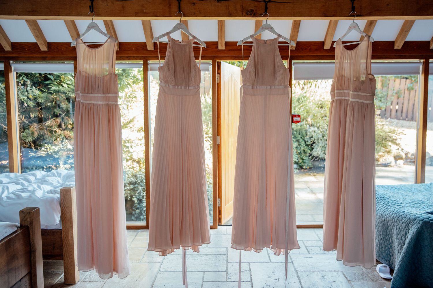 Row of blush pink bridesmaid dresses hanging in a rustic venue.