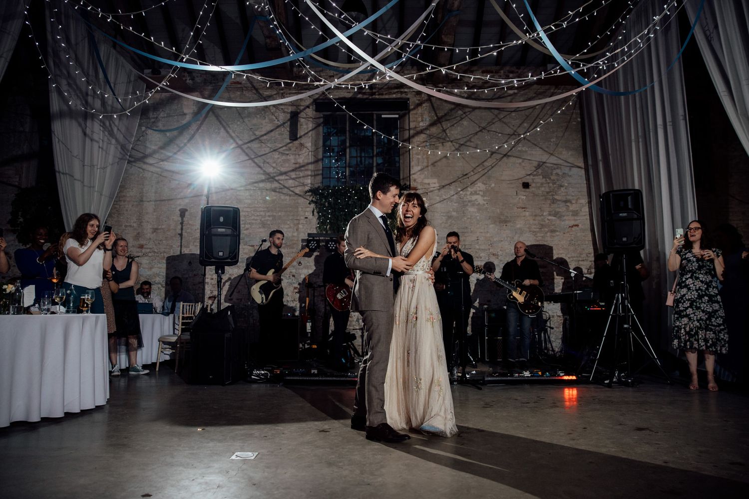 Evening wedding reception with guests dancing under twinkling lights and draped decor.