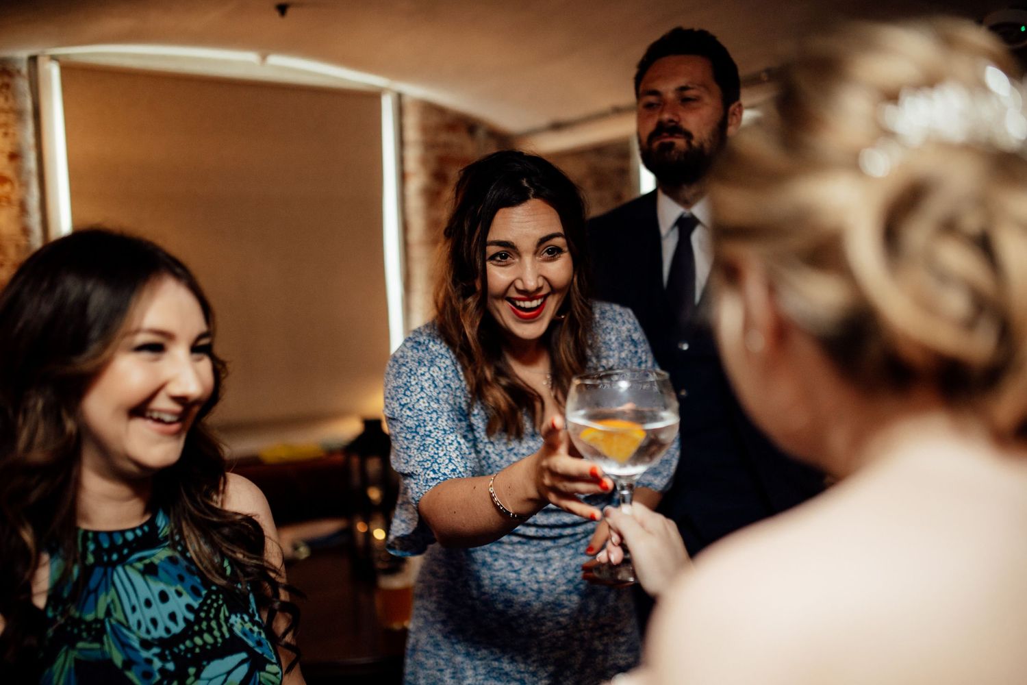 Wedding reception guests enjoying drinks and conversation in warm ambient lighting.