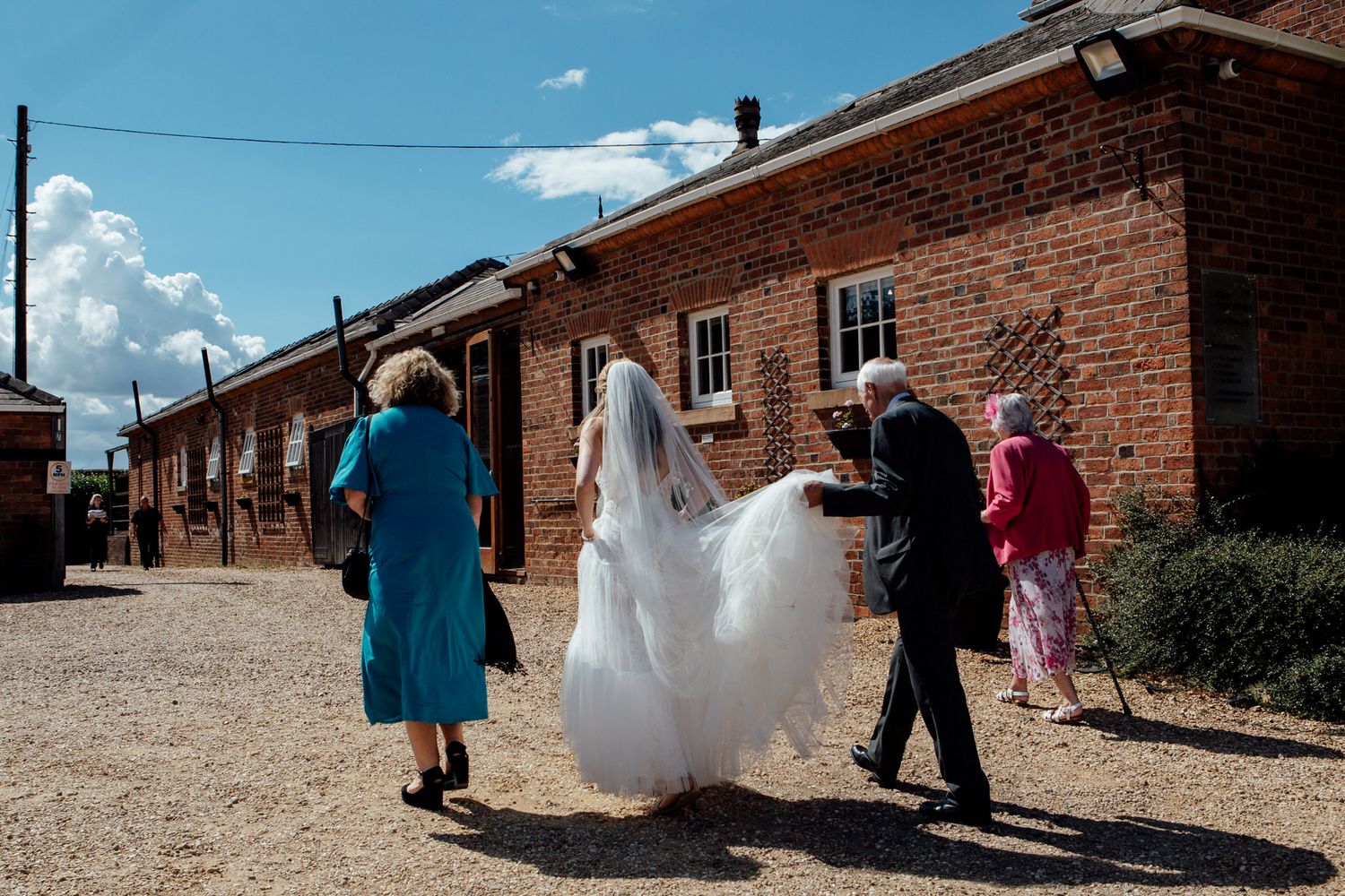 Wedding party walking along rustic brick buildings under blue sky.
