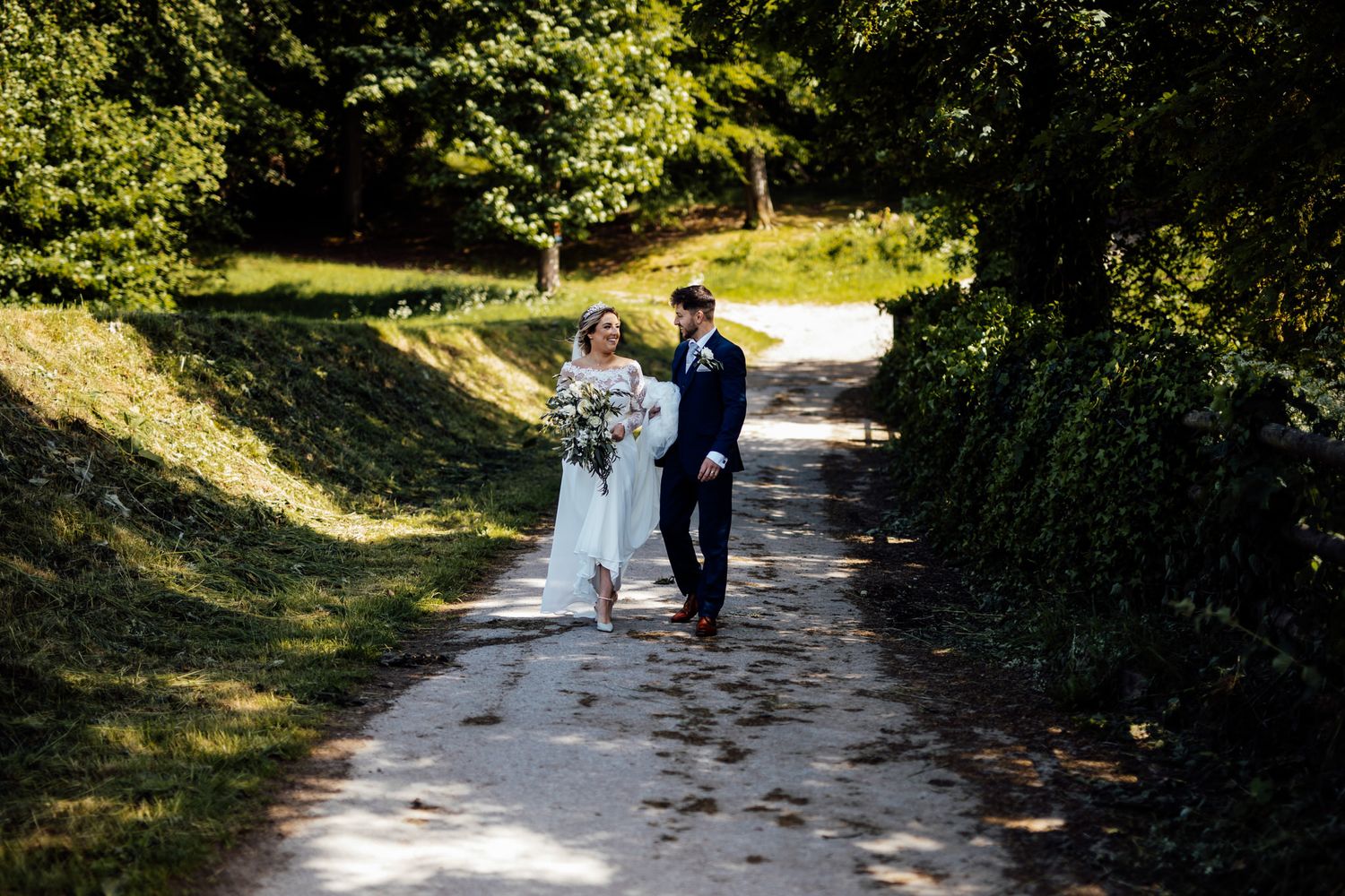 Tree-lined pathway with dappled sunlight creating a romantic outdoor wedding venue setting.