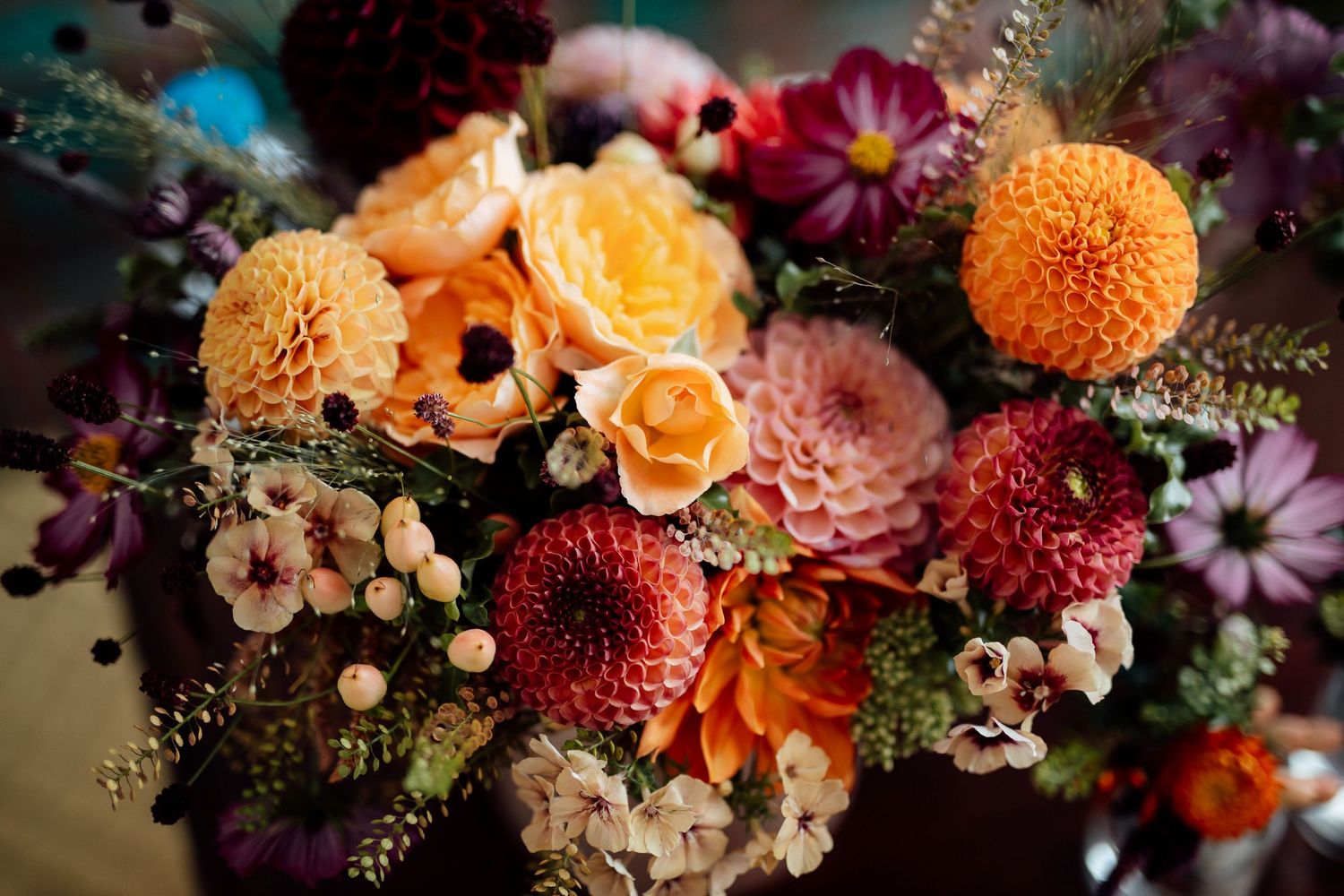 Vibrant floral arrangement features orange, red, and purple blooms in dramatic lighting.
