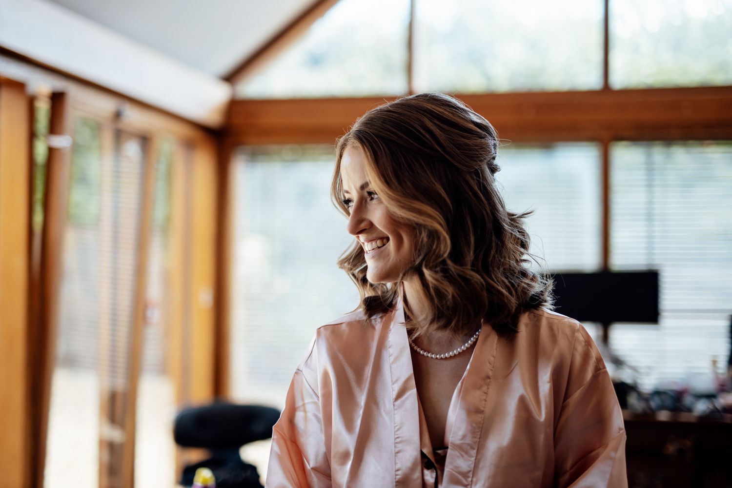 Bridesmaids in white robes laugh and smile together during wedding day preparations.