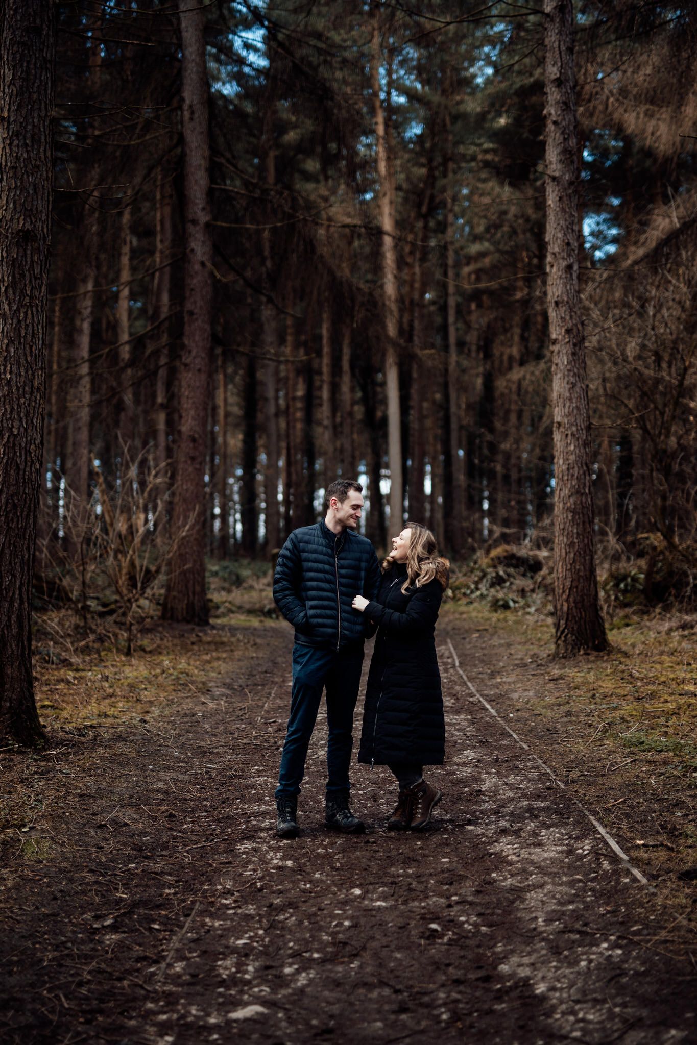 Romantic forest photography session with moody lighting and tall pine trees.