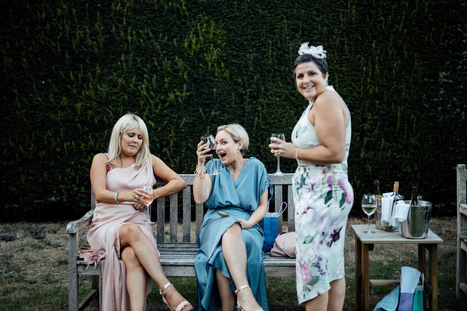 Wedding guests socializing on garden benches during outdoor reception.