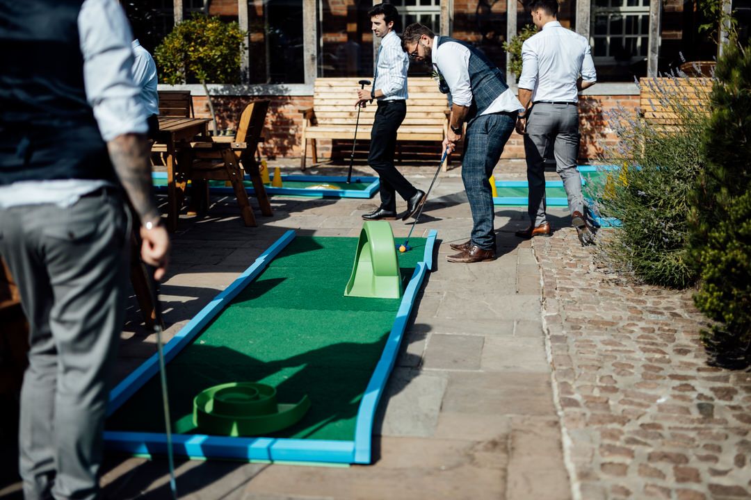 Wedding guests playing mini golf on a green outdoor course.