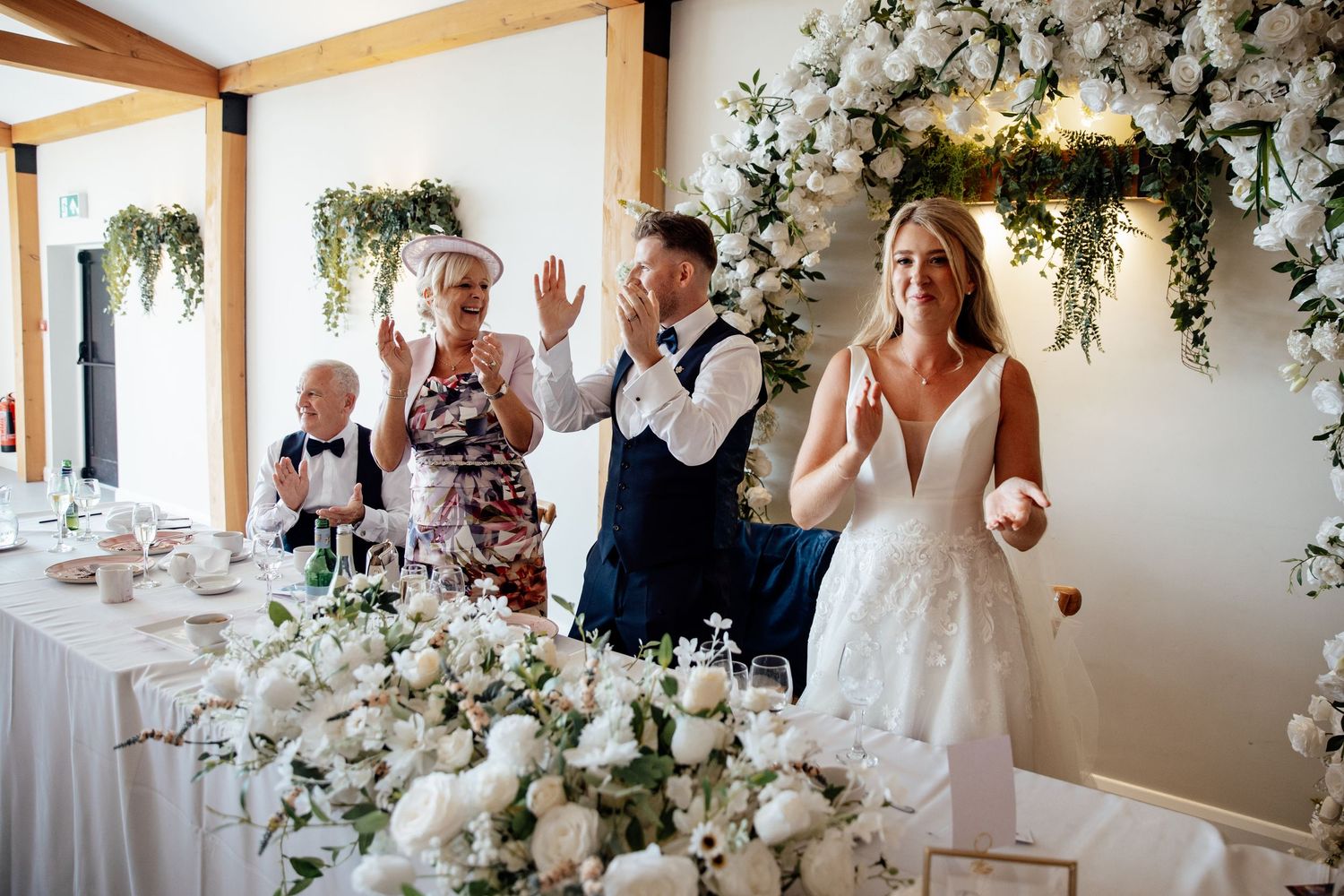 Elegant wedding reception room decorated with white floral arrangements and hanging greenery.