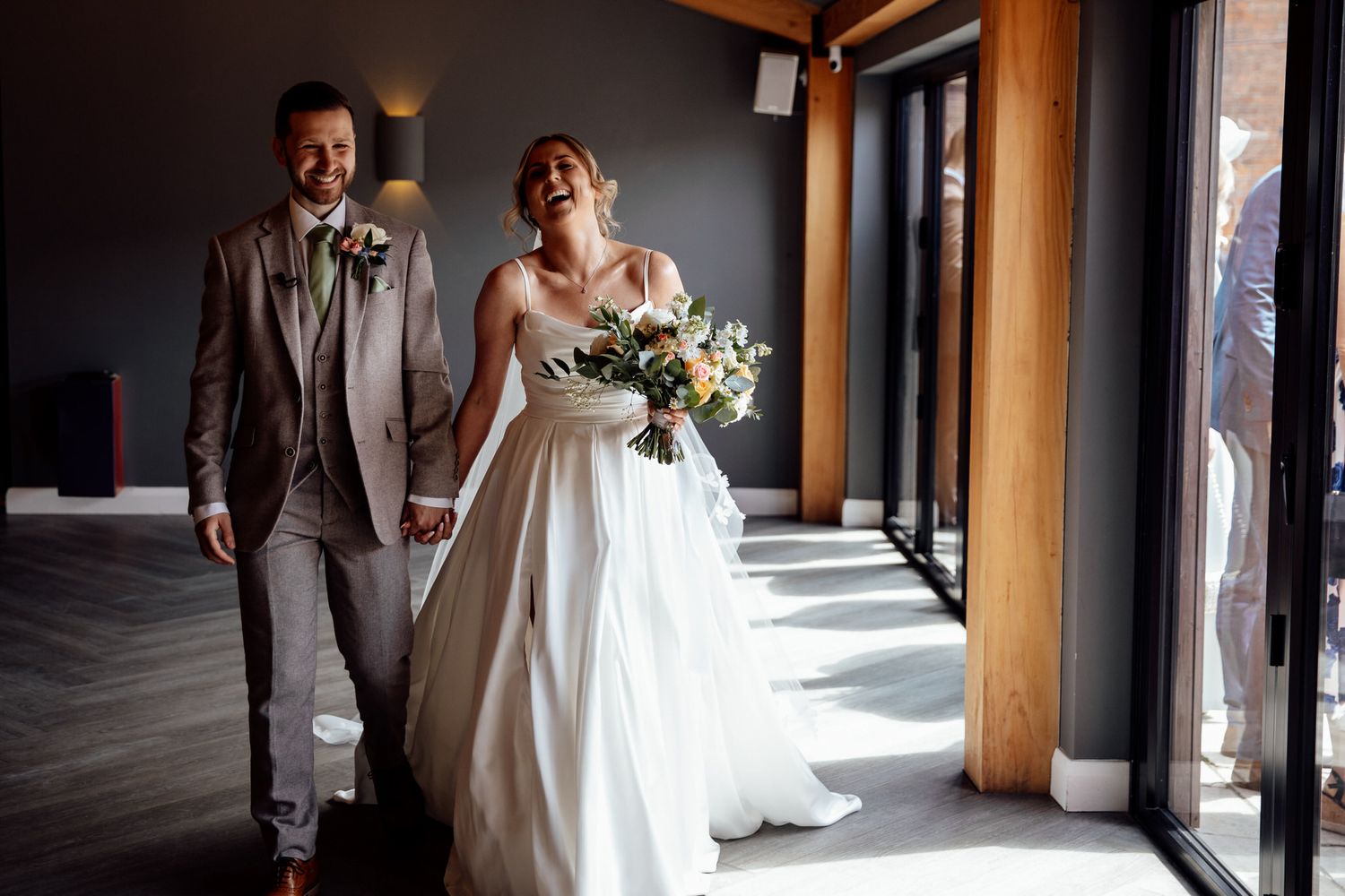 Couple walking together in sunlit hallway during wedding celebration.