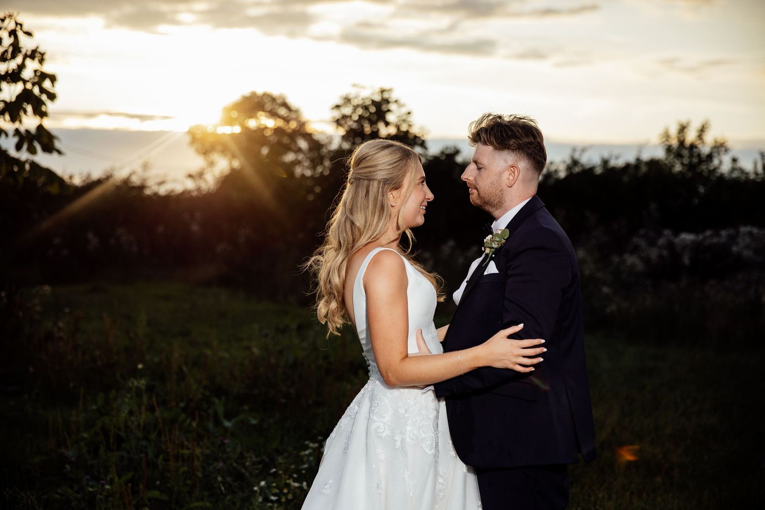 Newlyweds embrace during golden hour sunset photo session in garden setting.