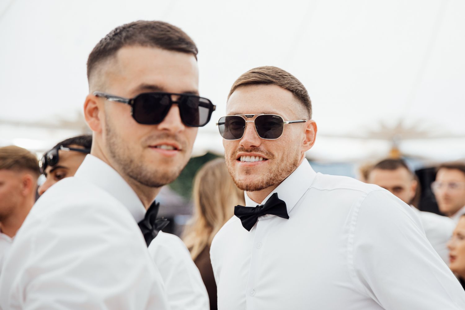 Wedding guests in white shirts and sunglasses pose together at an outdoor celebration.