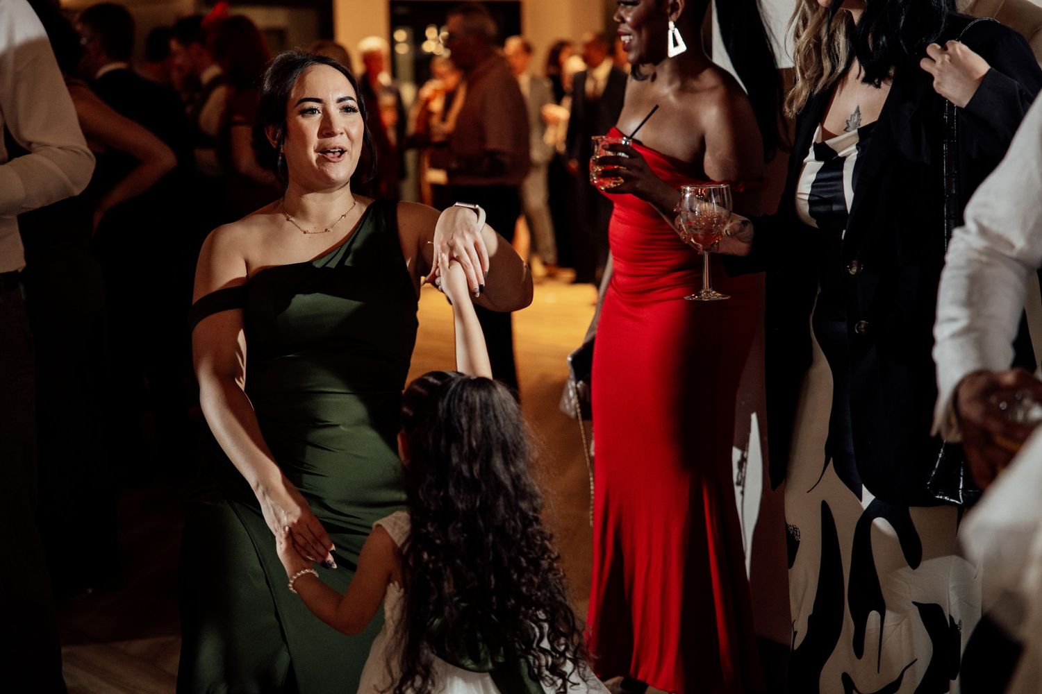 Wedding guests in elegant green and red gowns dance and celebrate joyfully at evening reception.