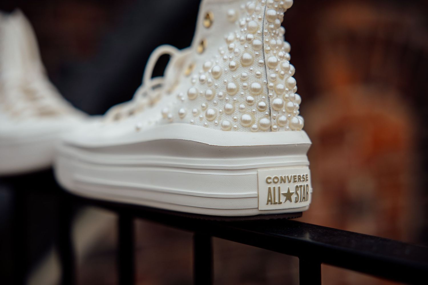 White pearl-studded Converse All Star high-top sneakers displayed on a black metal rack.