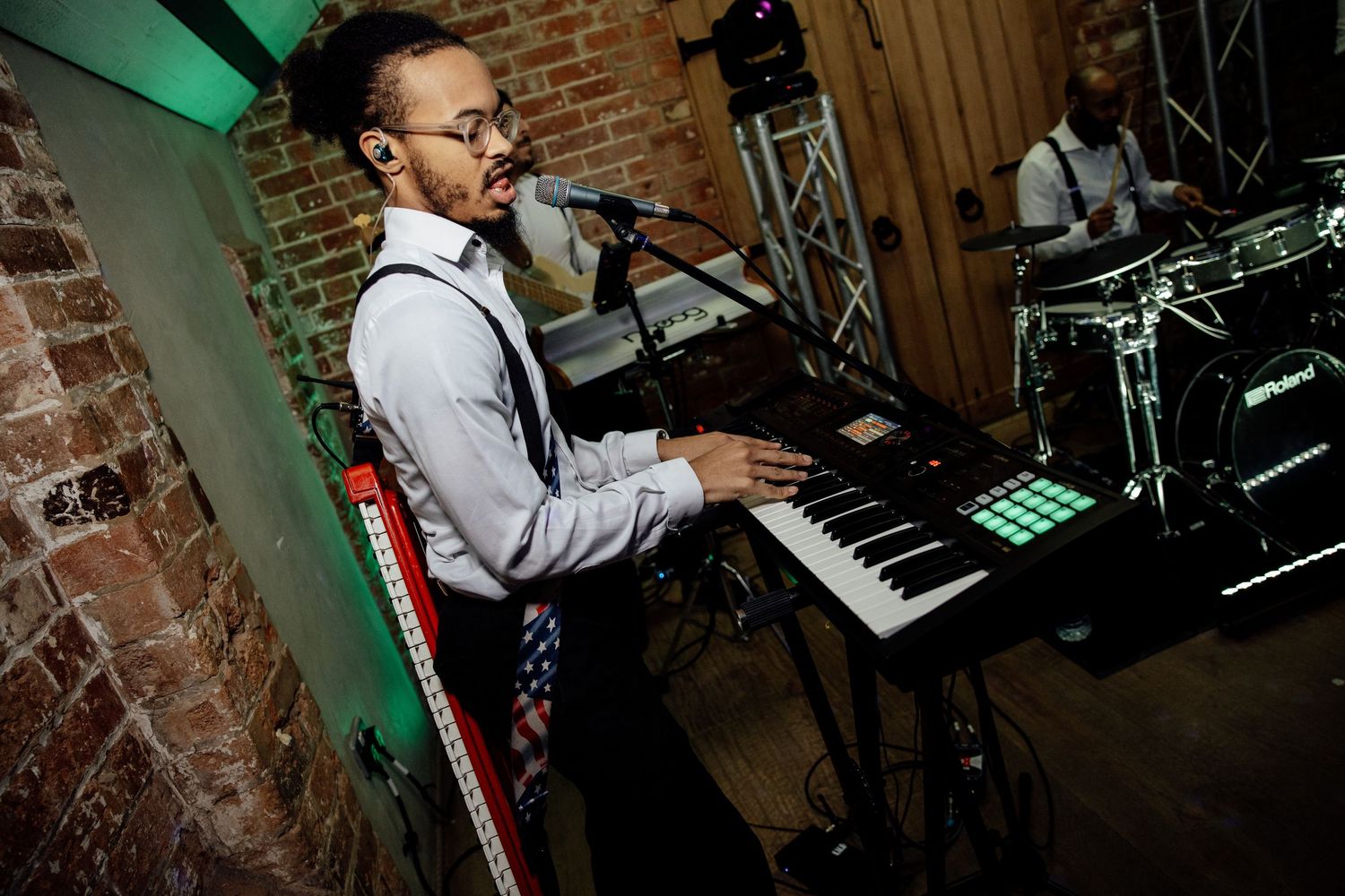 Musicians performing at wedding reception with keyboard and instruments in rustic brick venue.