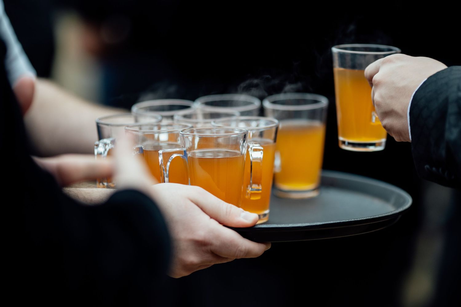 Row of beer glasses being served on a dark wooden bar surface.