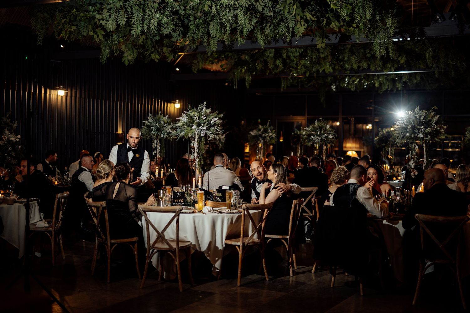 An outdoor evening wedding reception with string lights illuminating tables and guests.