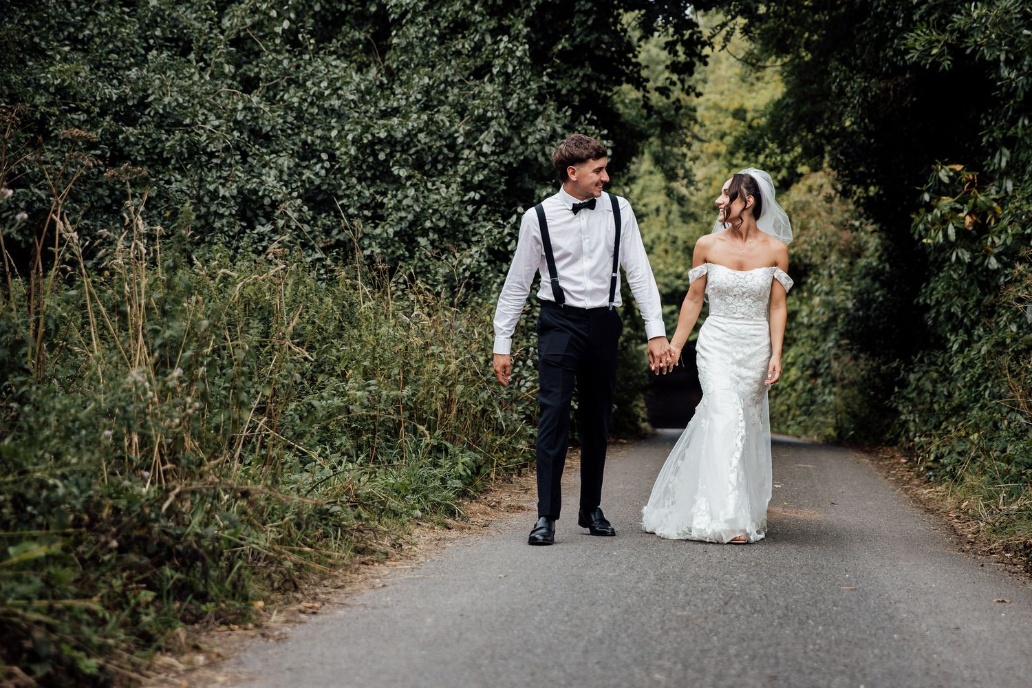 A couple walks hand in hand down a country lane on their wedding day.