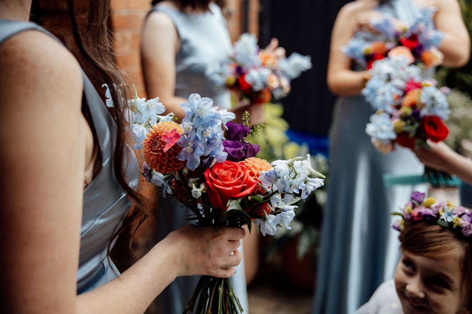 Vibrant blue and coral floral bouquets held during outdoor wedding ceremony.