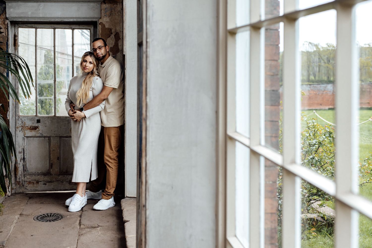 A couple embraces in a sunlit industrial space with white walls and large windows.