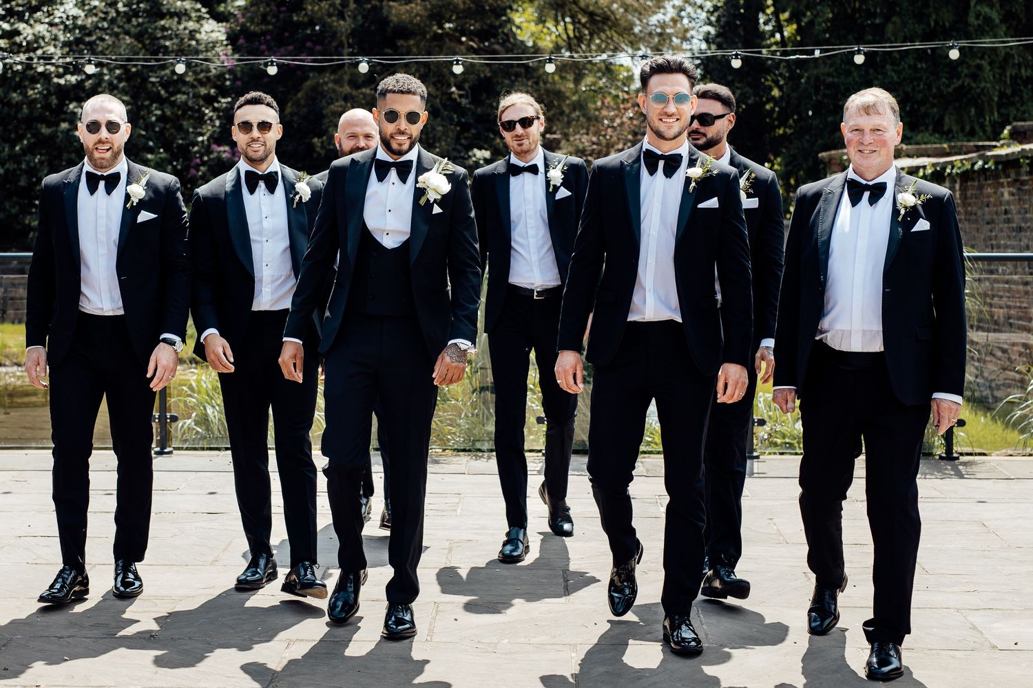 Groomsmen in classic black tuxedos pose together for formal wedding photos.