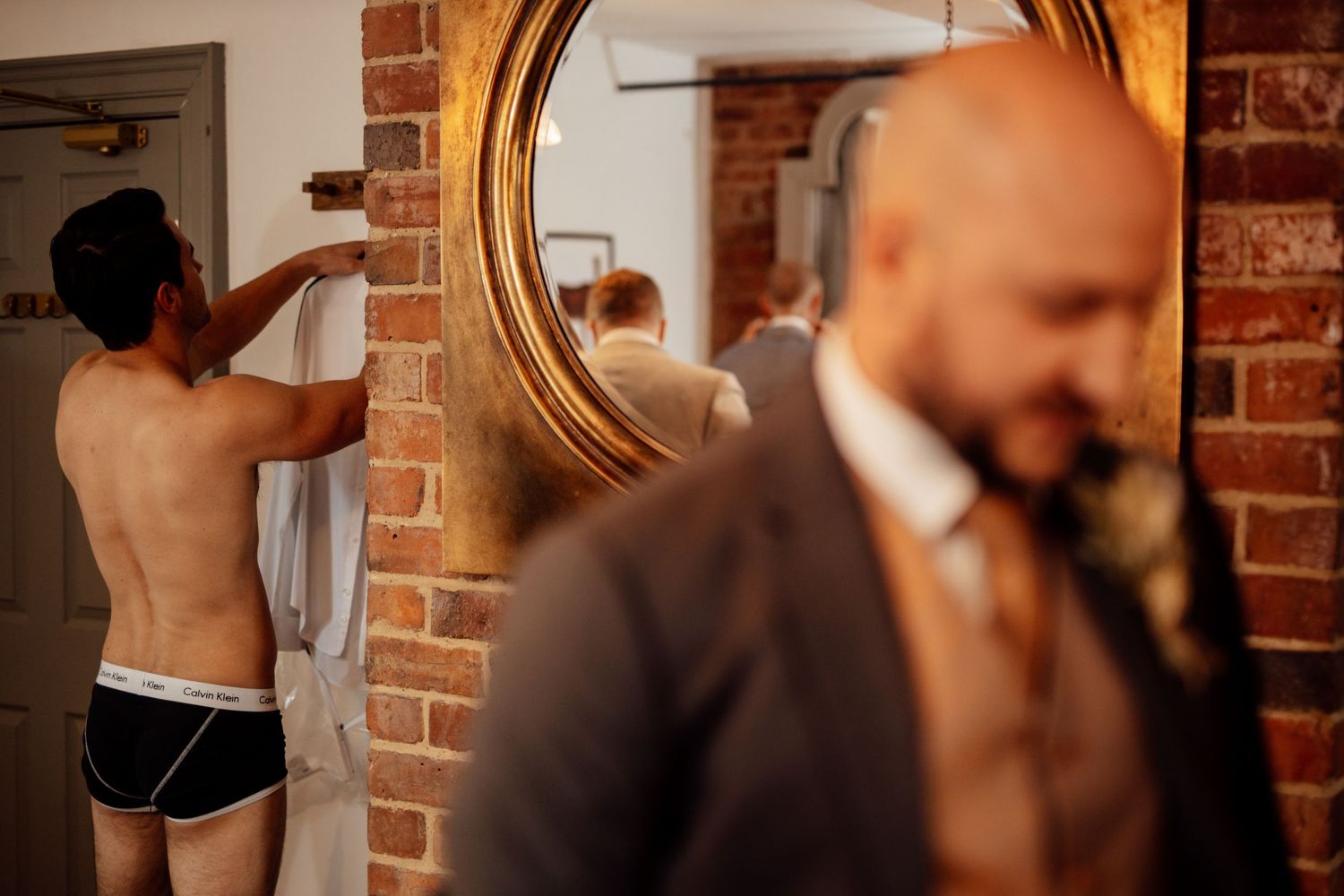Intimate wedding moment captured against rustic brick wall with warm lighting.