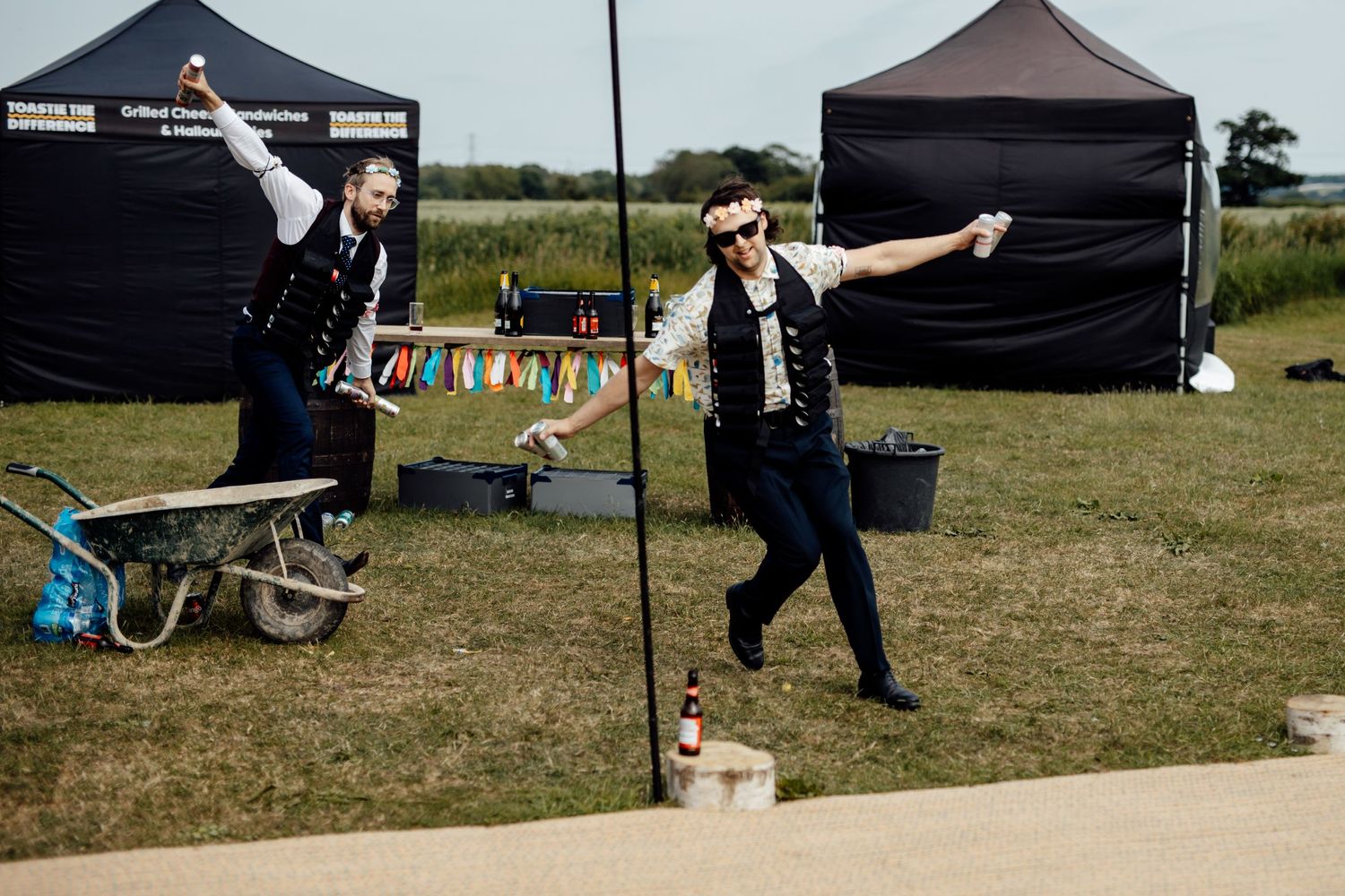 Two performers in dark outfits striking dramatic poses outdoors near festival tents.