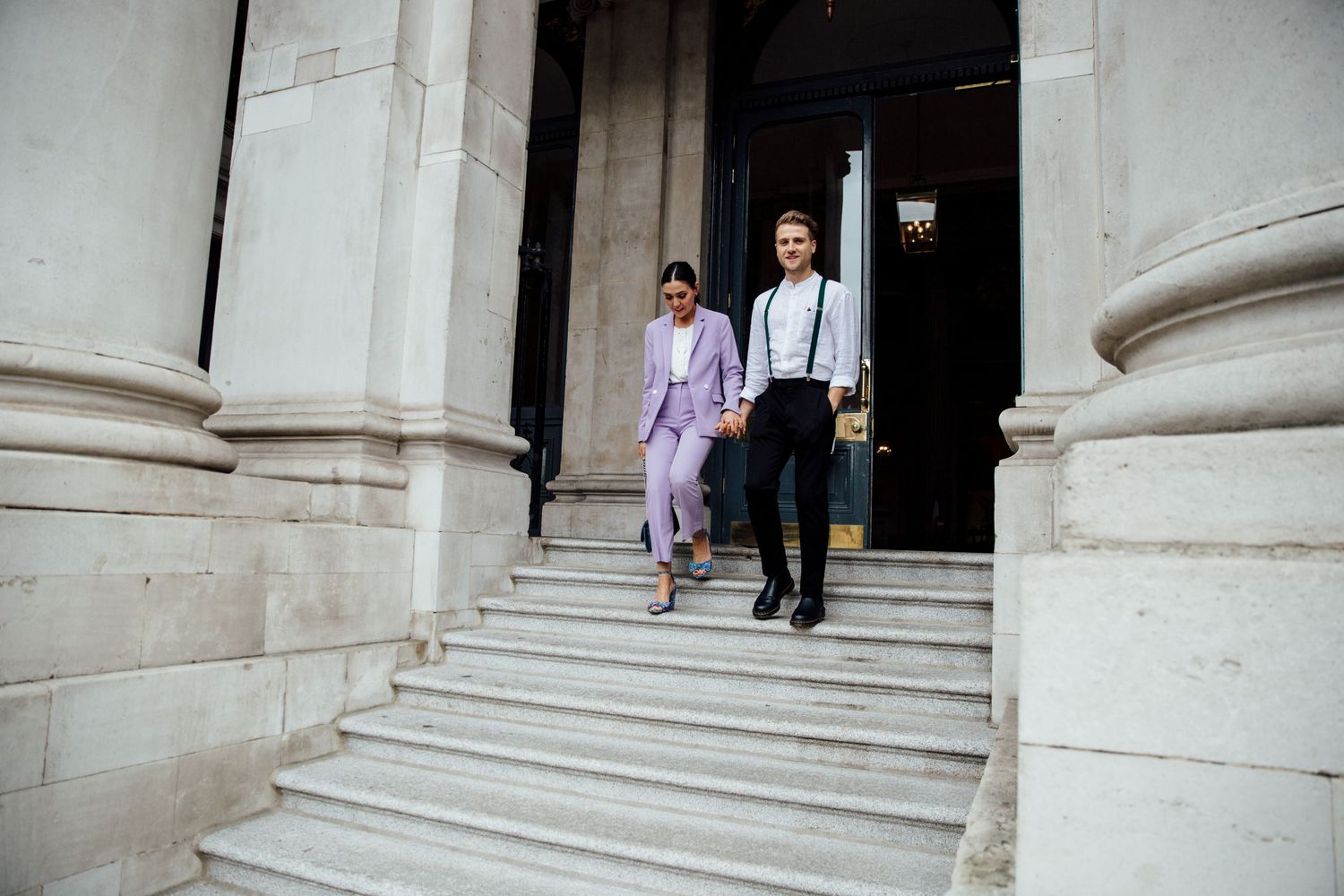 People walking down white stone steps of a grand building entrance.