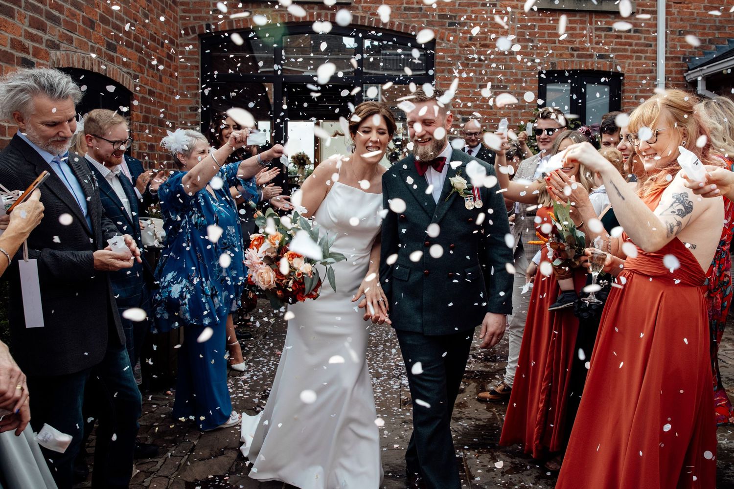 Wedding guests throwing white confetti outside brick church during celebration exit.
