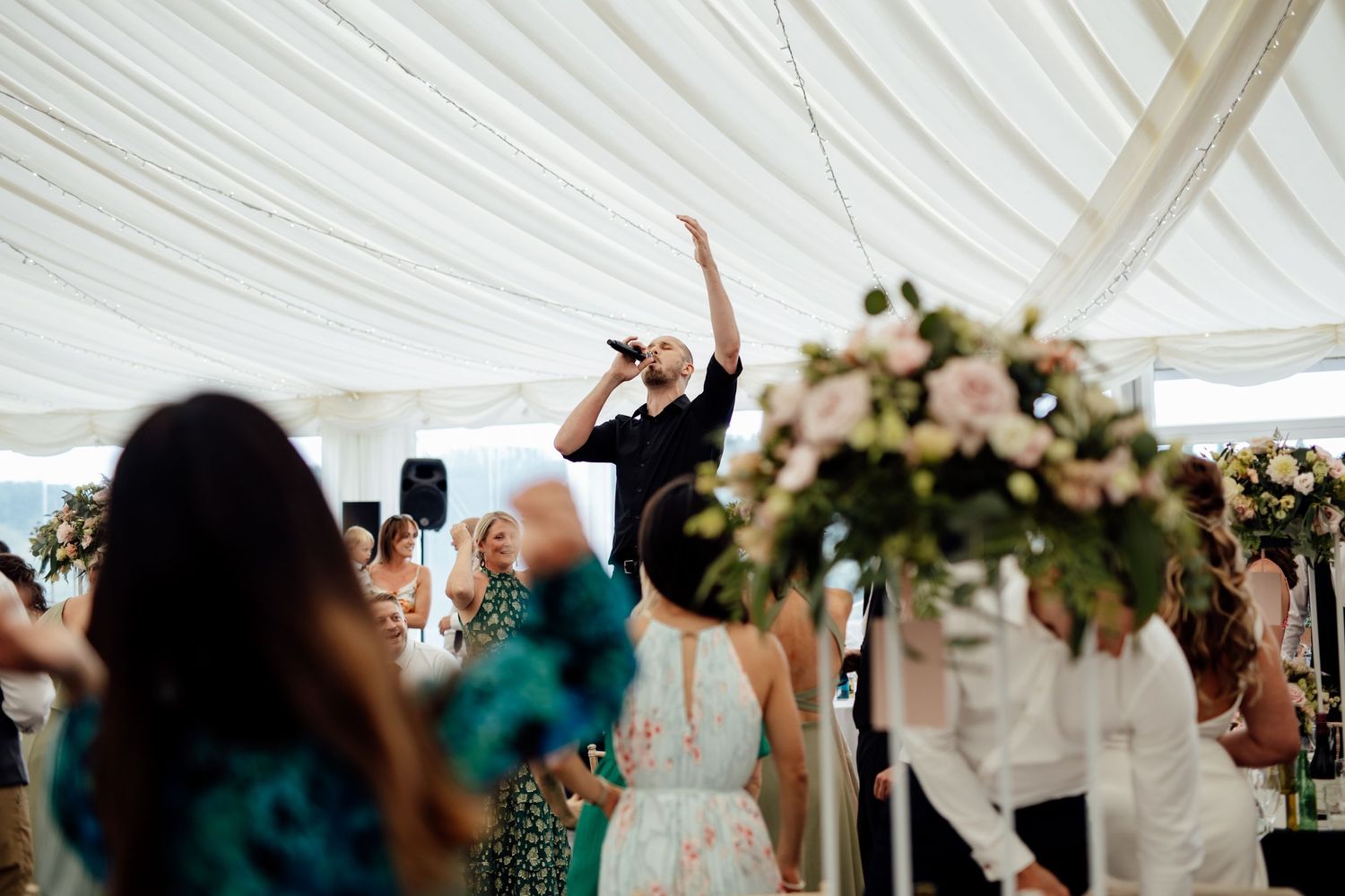 Celebration under a white tent with guests dancing and raising their hands.