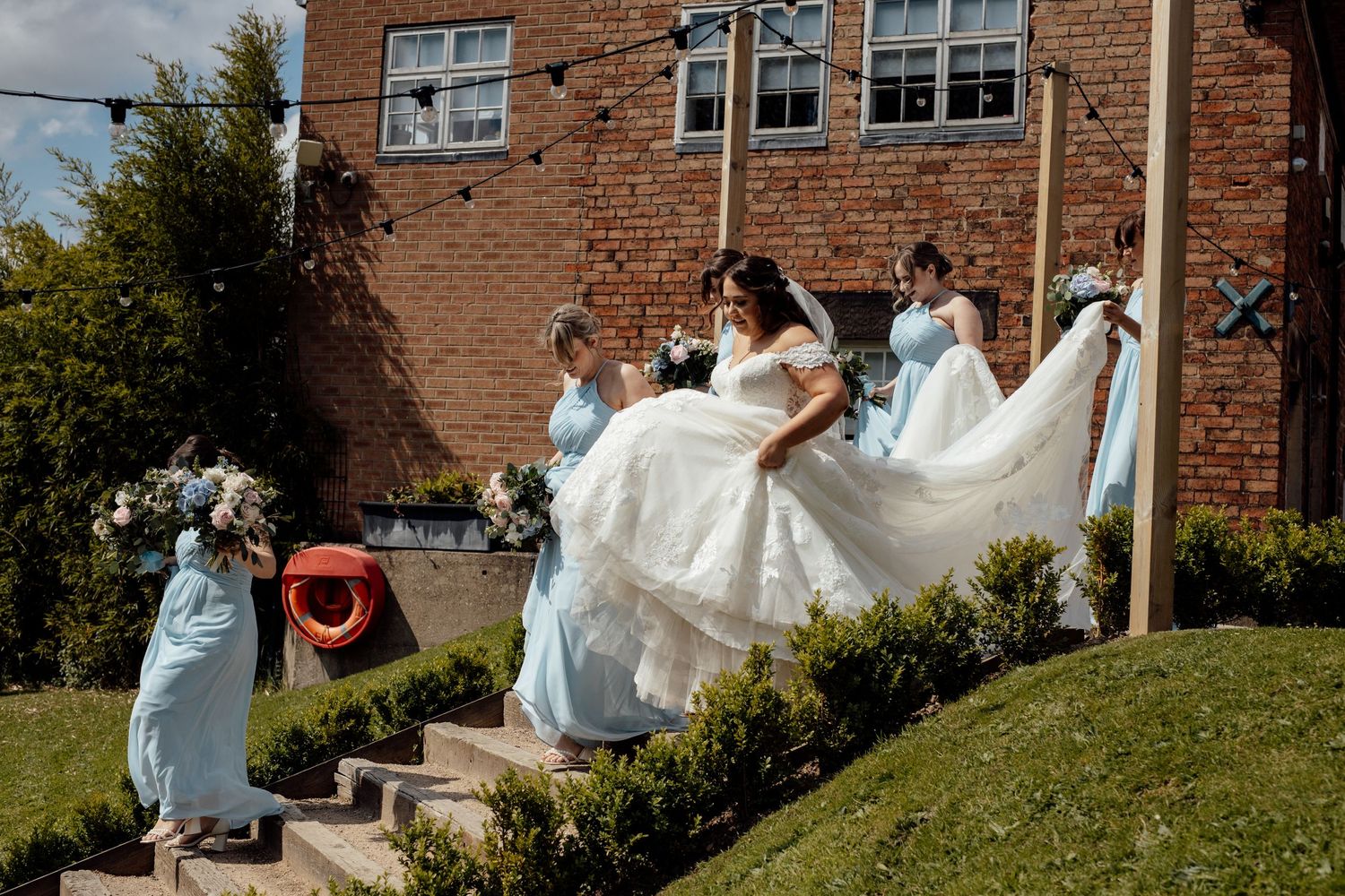 Wedding party having fun with dress photos outdoors by brick building.