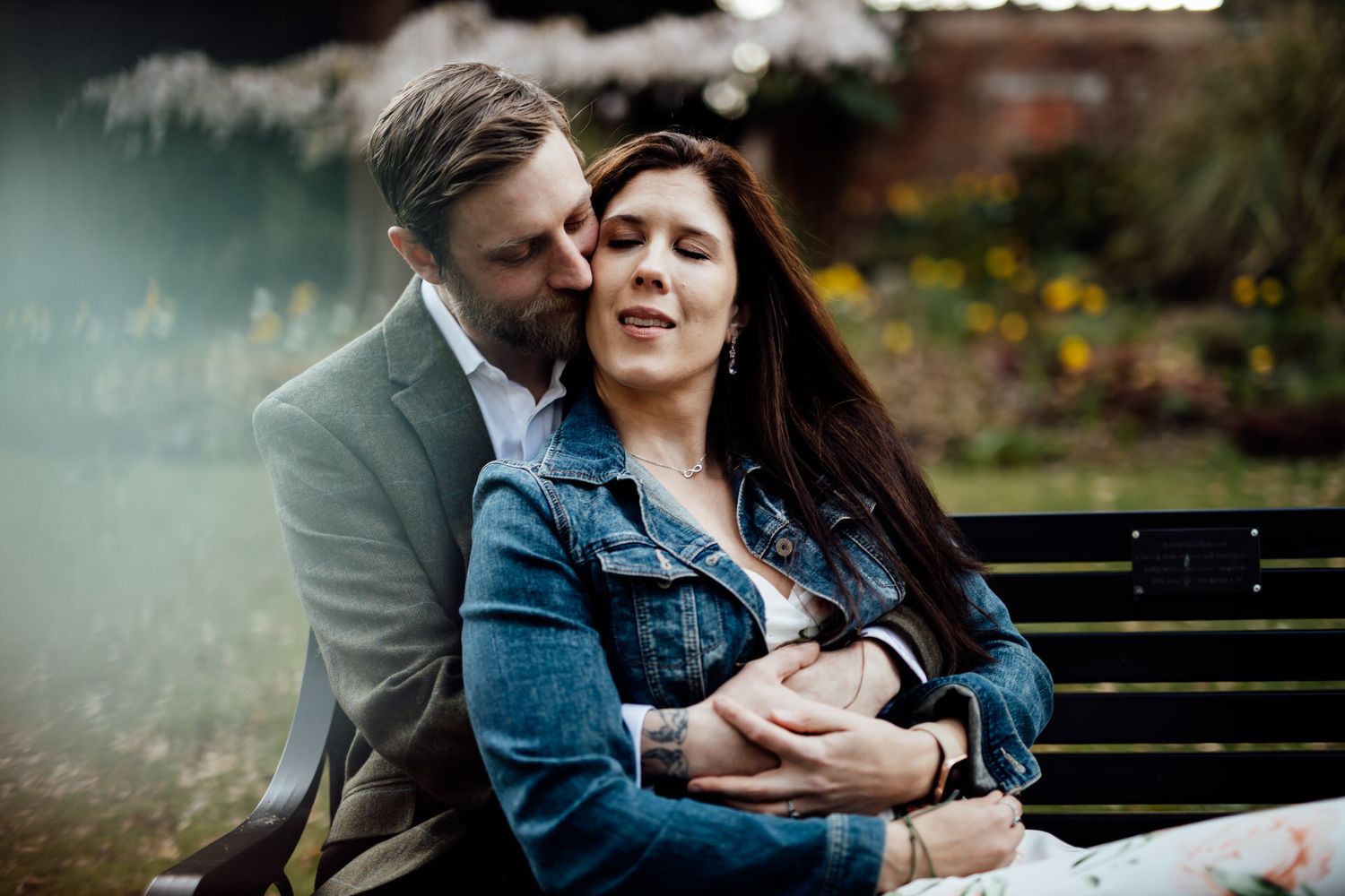 Couple sitting close together on wooden bench in natural outdoor setting.