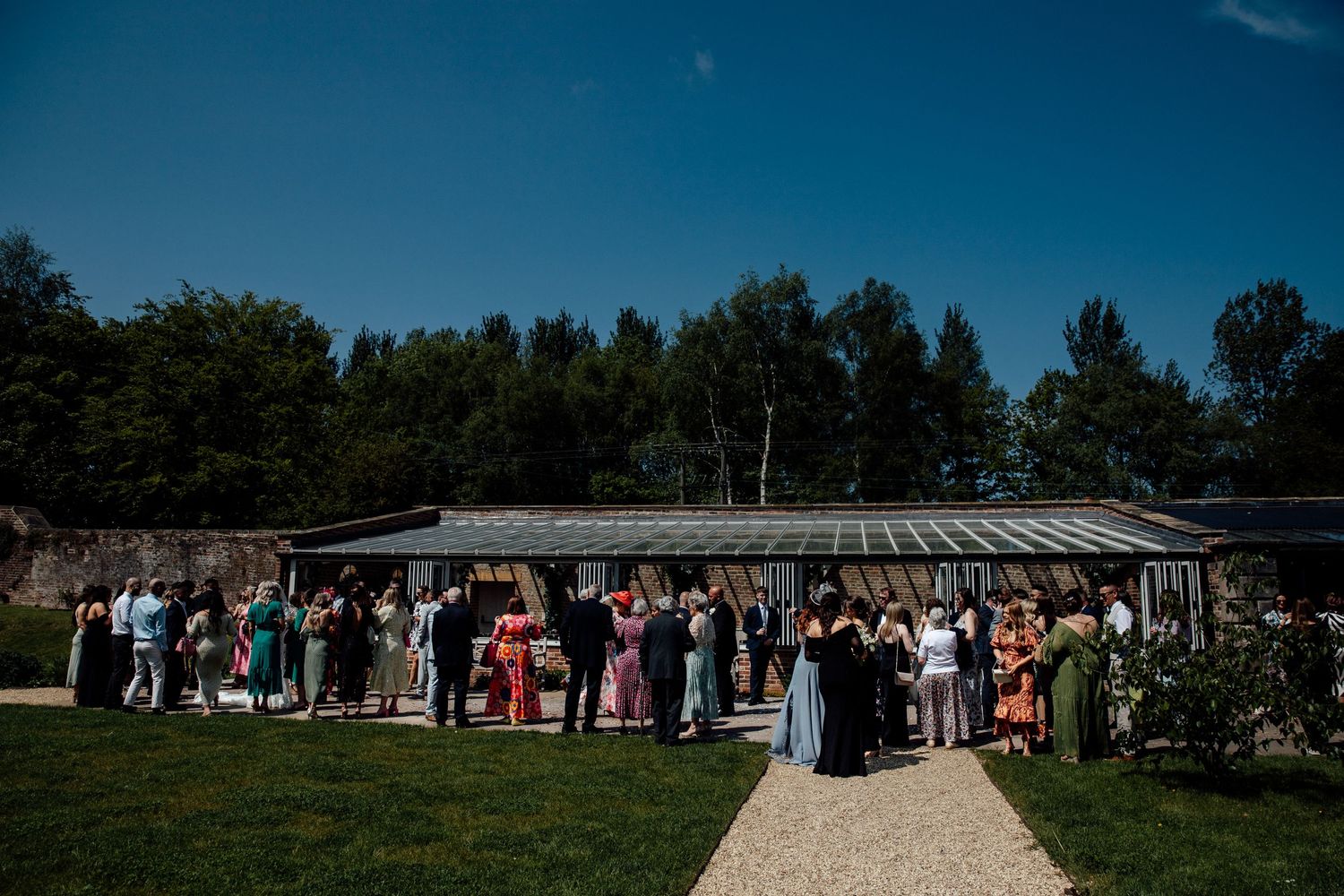 Wedding guests gather outside a rustic venue under bright blue skies.