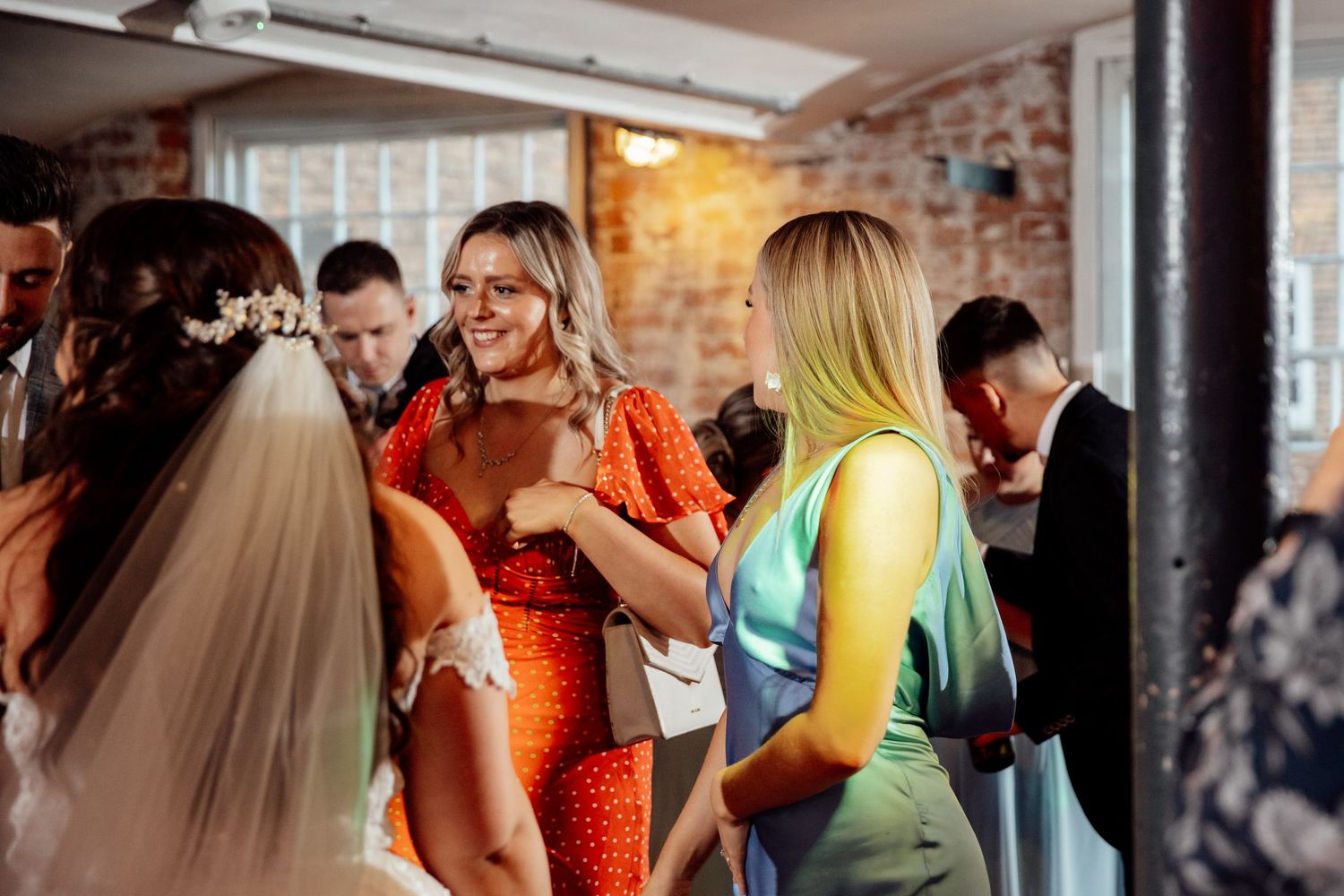 Wedding reception guests dancing in a rustic brick-walled venue with ambient lighting.
