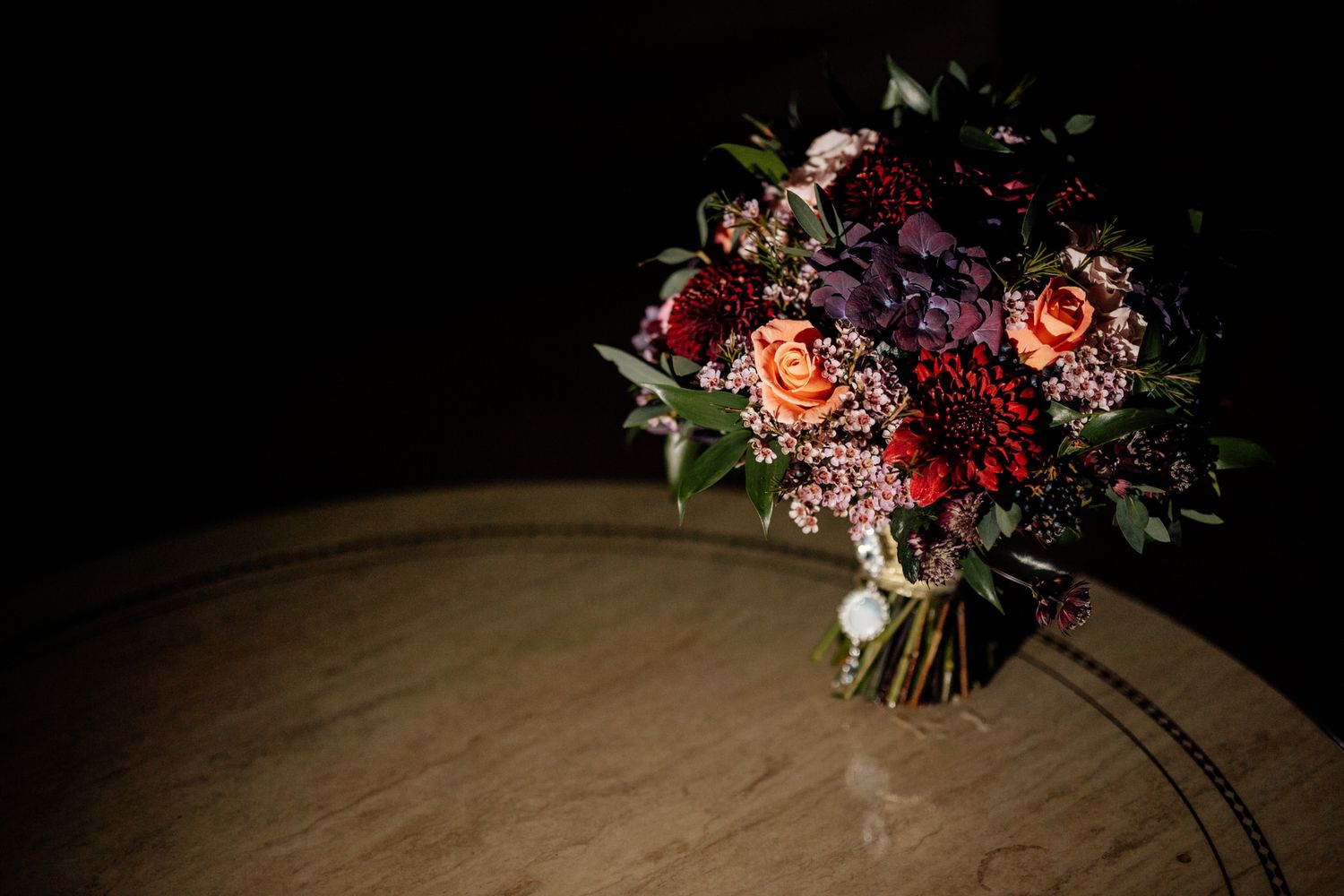 Vibrant burgundy and coral wedding bouquet displayed against dark background.