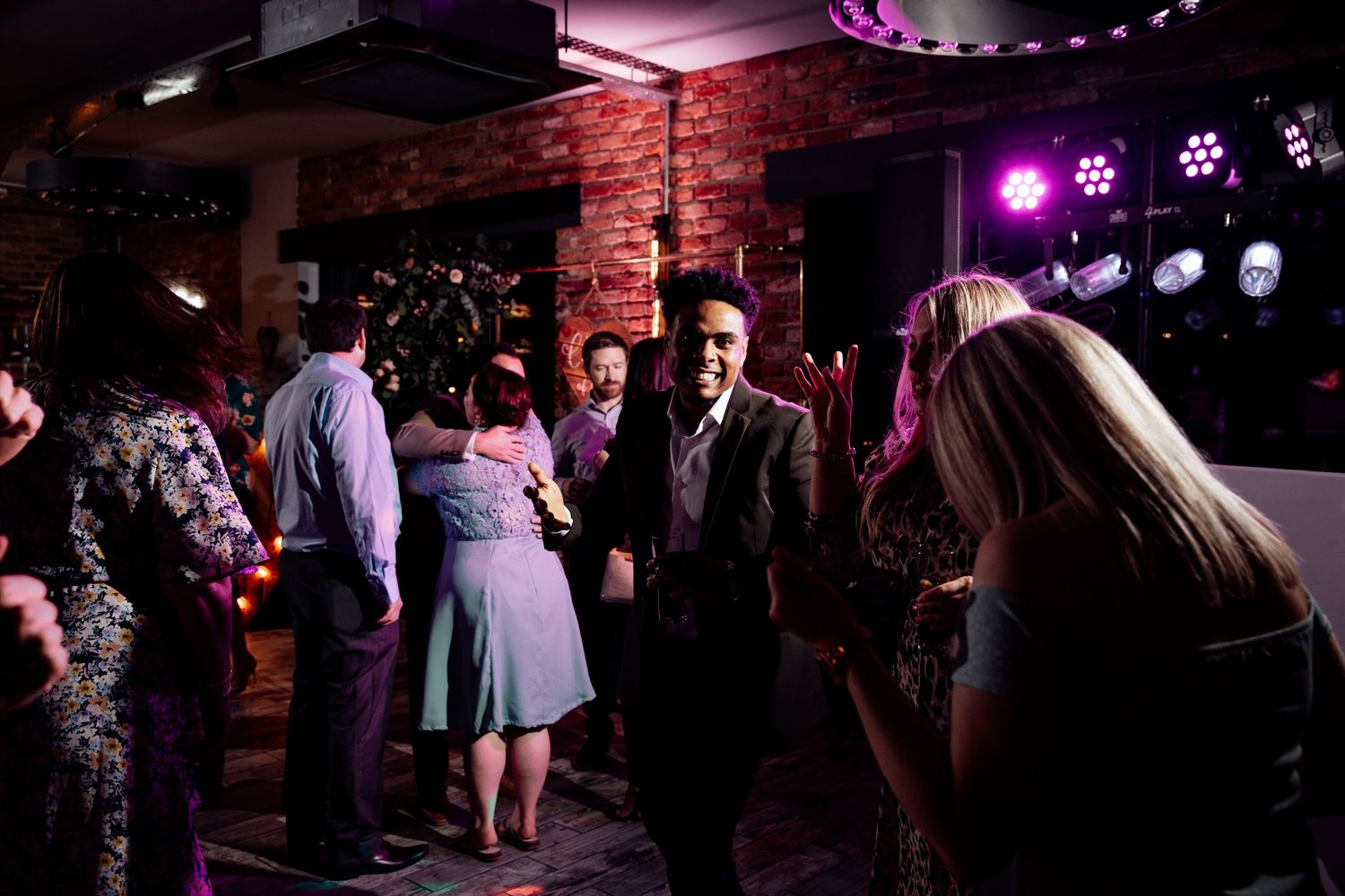 Purple and pink mood lighting illuminates a dance floor at an evening wedding reception.