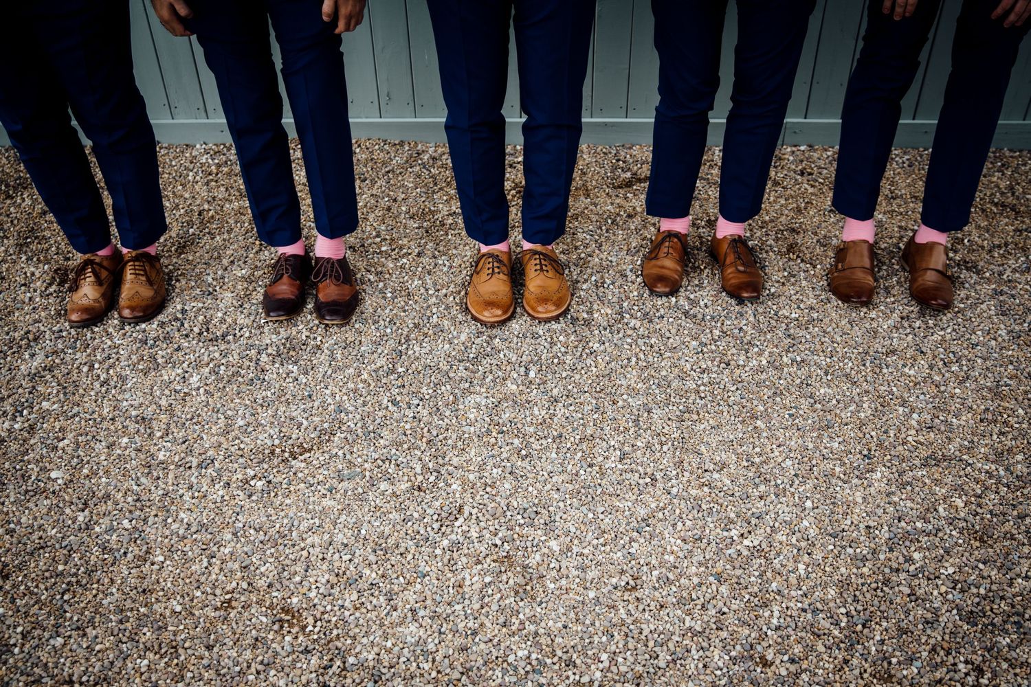 Row of dress shoes and boots lined up on gravel at outdoor wedding.