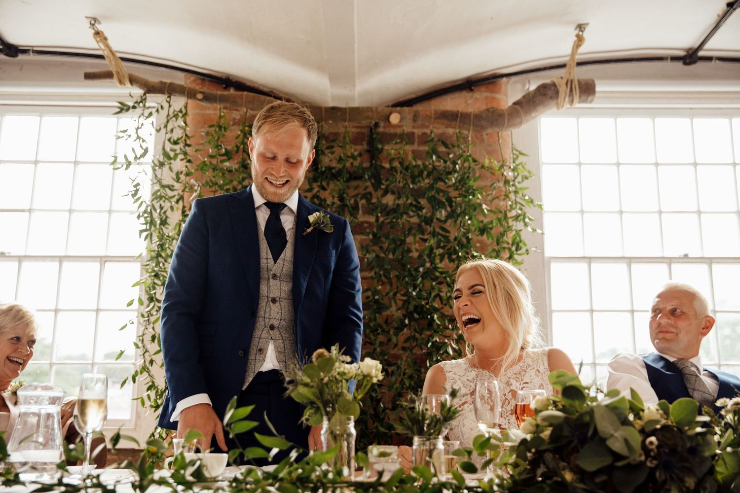 Wedding reception guests toasting during speeches in sunlit venue.