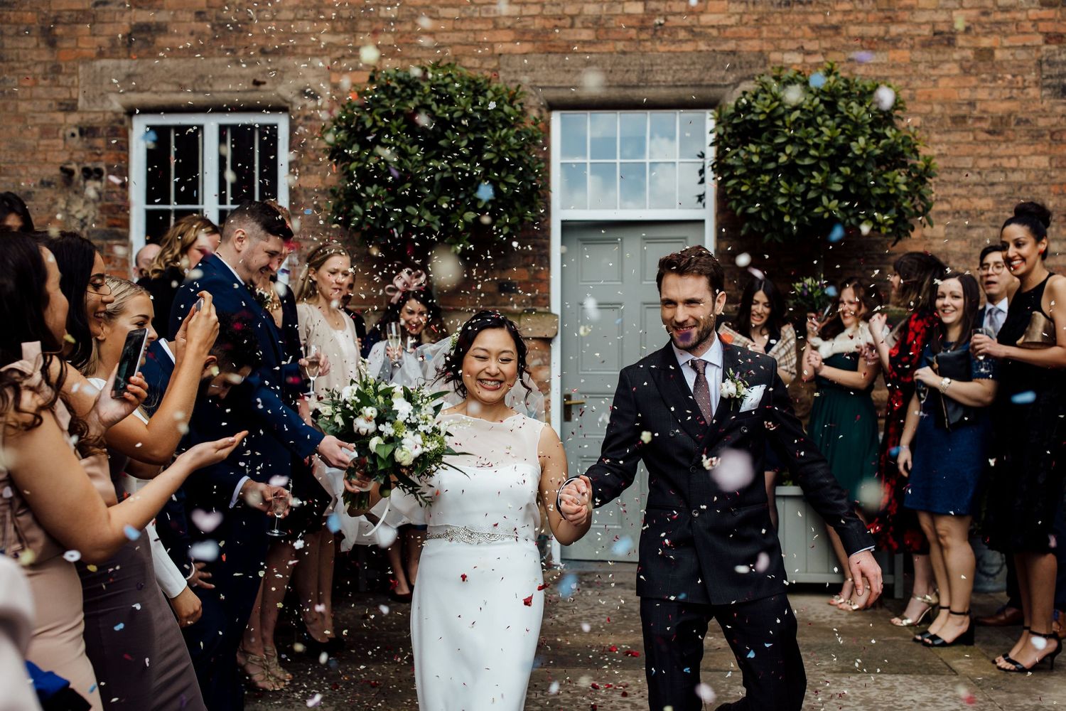 Newlyweds exit venue while guests throw confetti in celebration.
