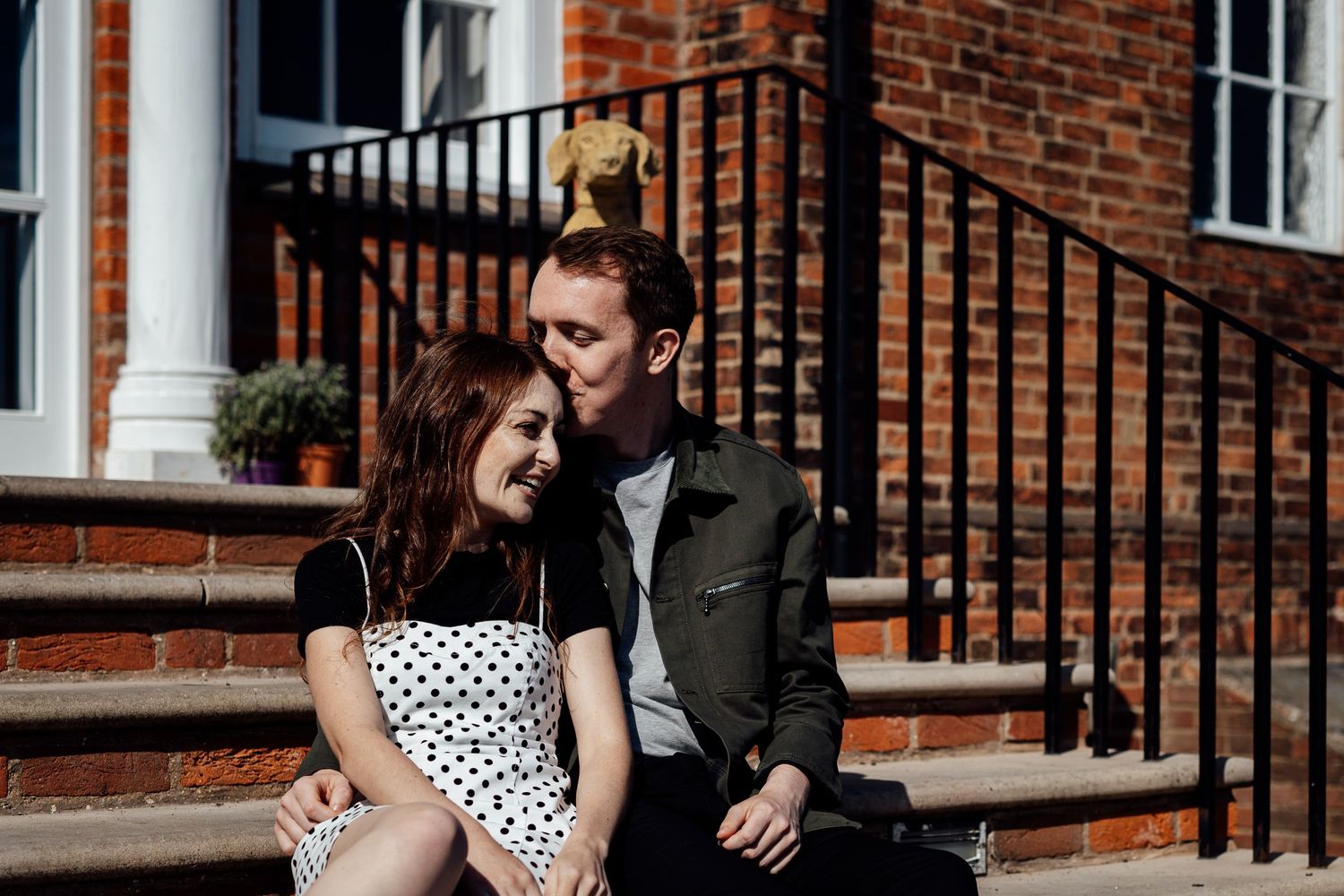 A couple sits on brick steps in front of a traditional red brick building.